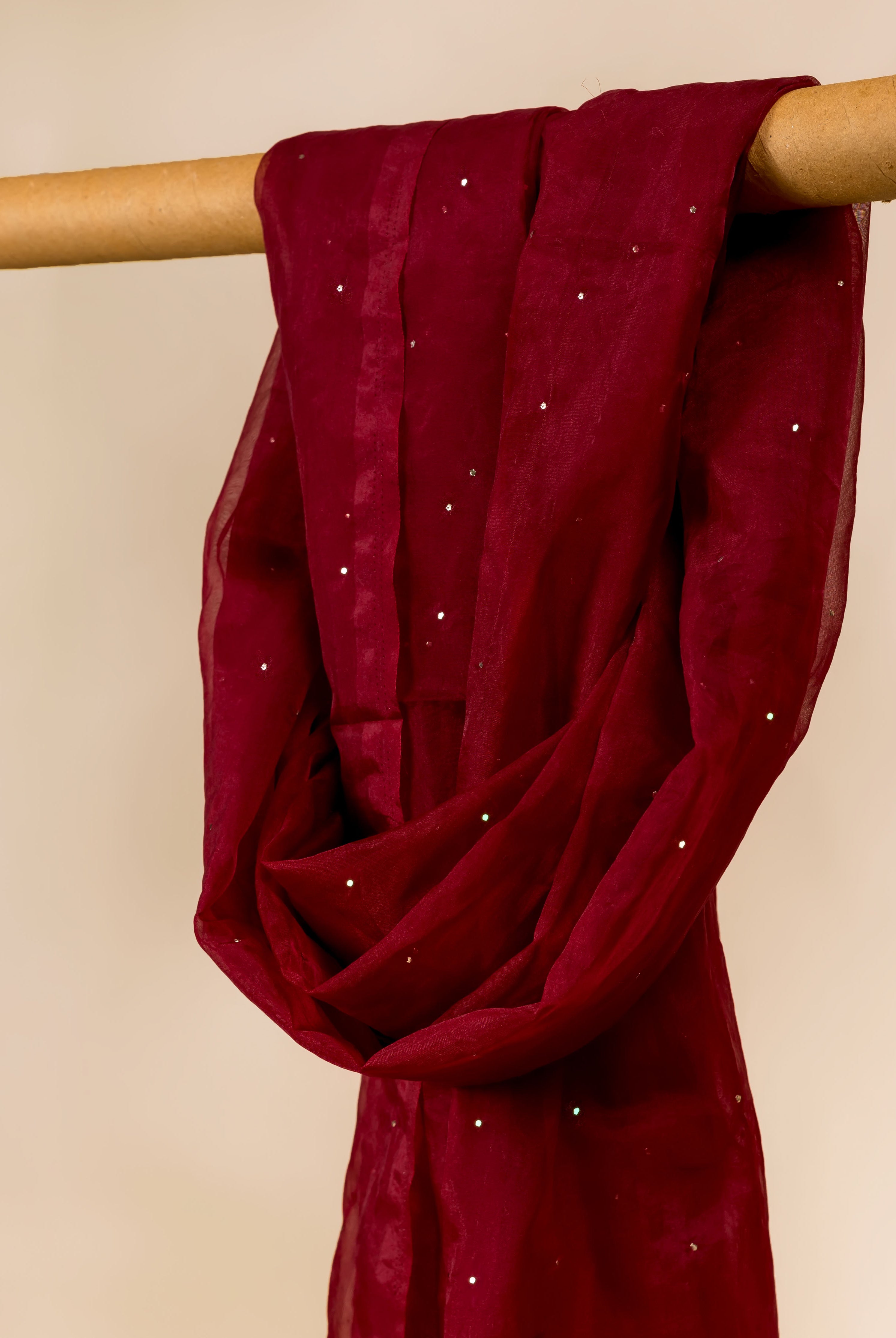 Close-up of a maroon organza dupatta with scattered silver mukaish, draped on a wooden rod.