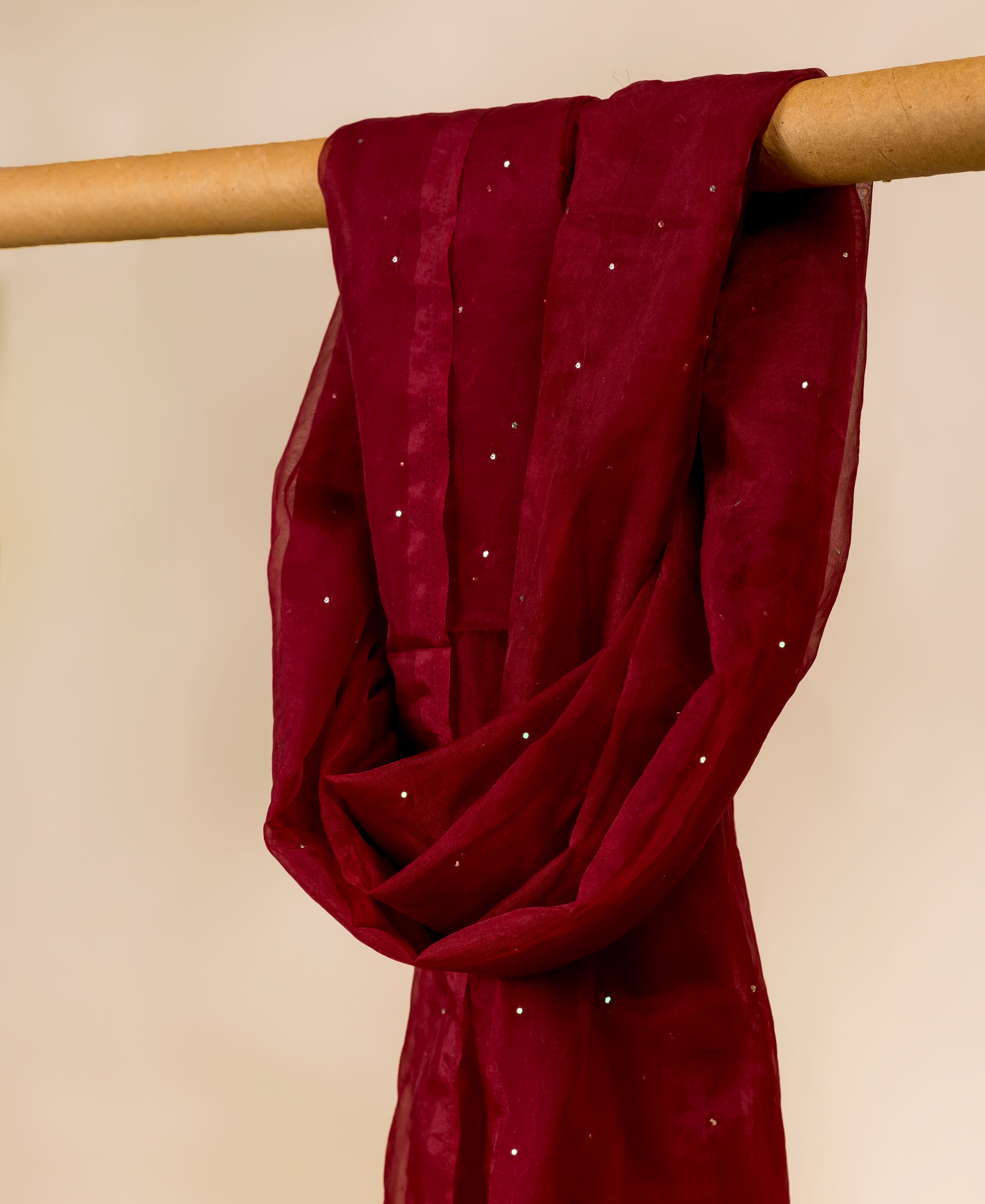 Close-up of a maroon organza dupatta with scattered silver mukaish, draped on a wooden rod.