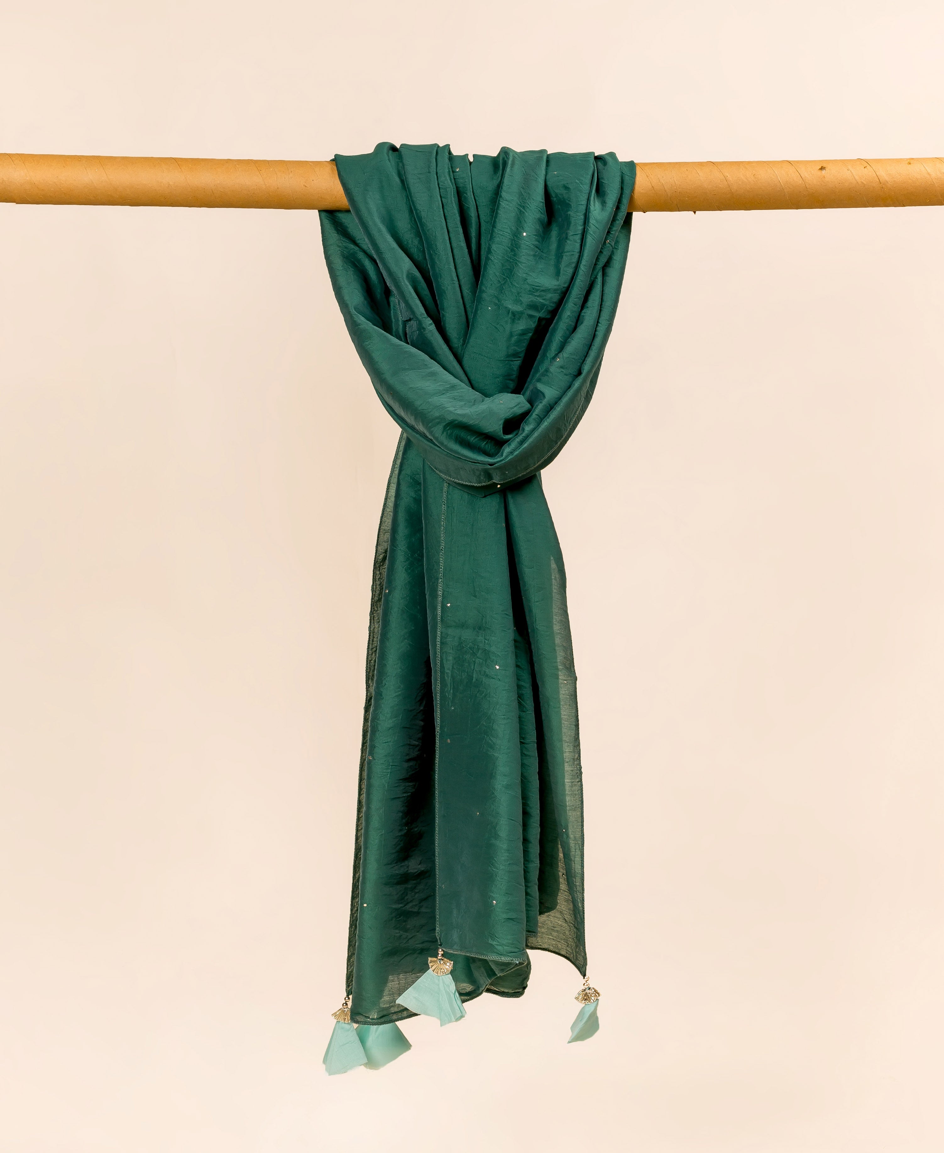 Teal green dupatta with shiny mukaish dots and light blue tassels, draped on a rod.