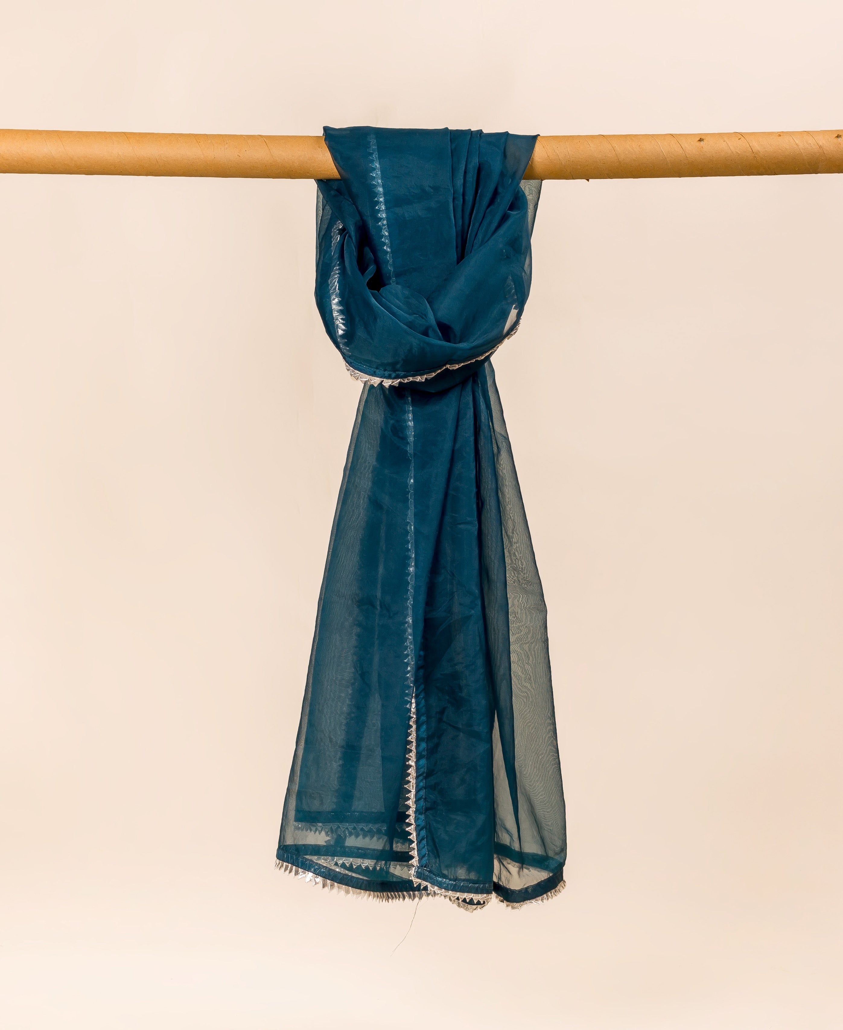 Teal blue organza dupatta with white trim, draped over a wooden pole.