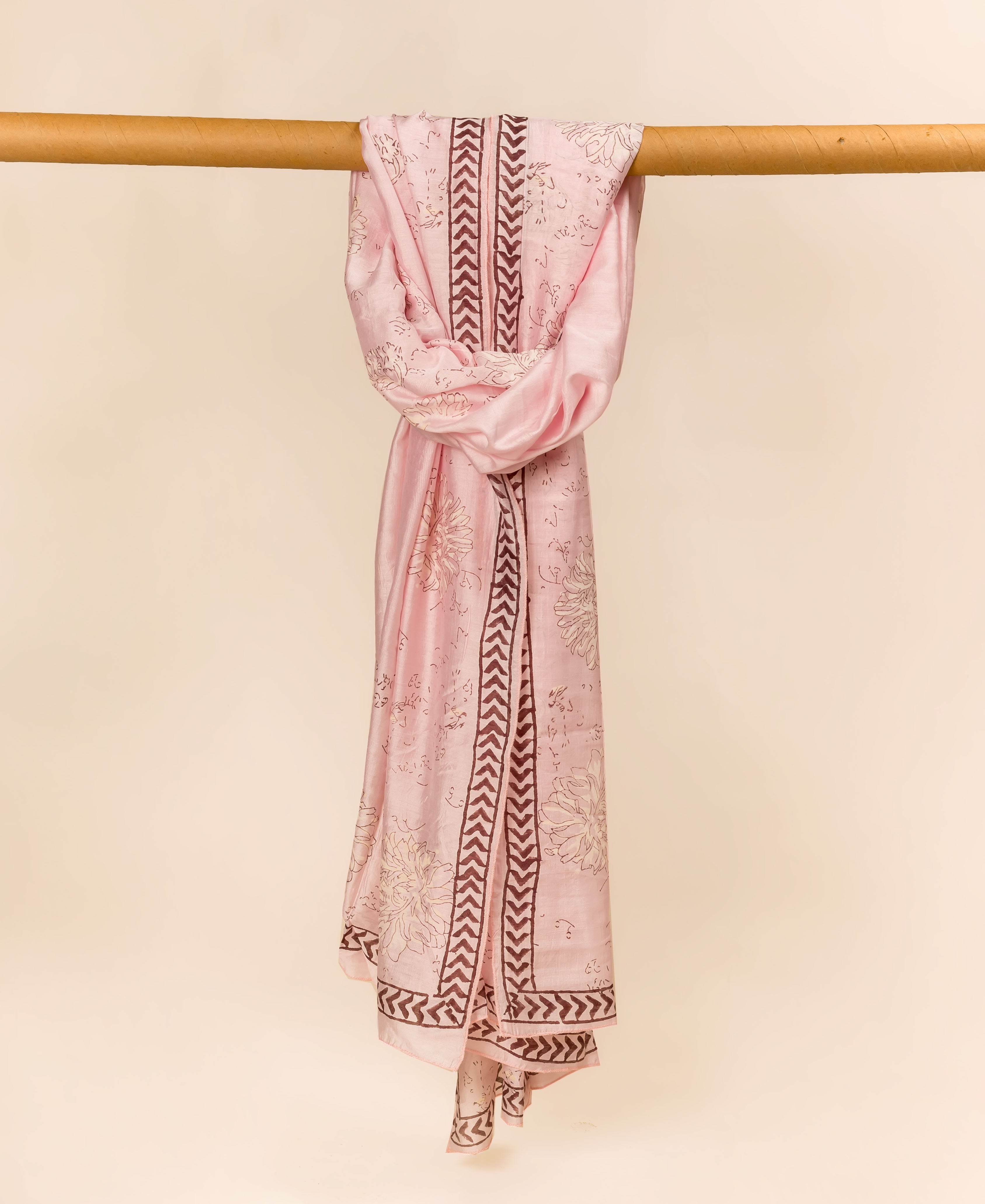 Blush pink hand block printed dupatta draped over a rod, with floral and brown chevron prints.