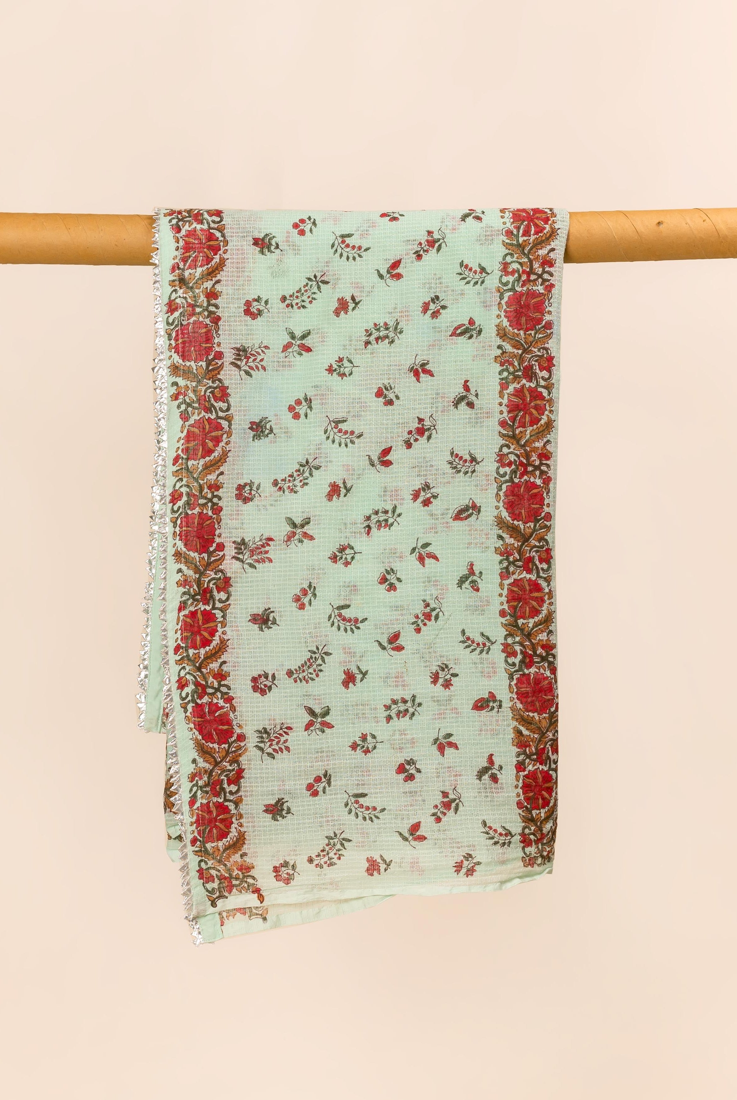 Mint green hand block printed dupatta with red floral designs and silver trim, draped on a rod.