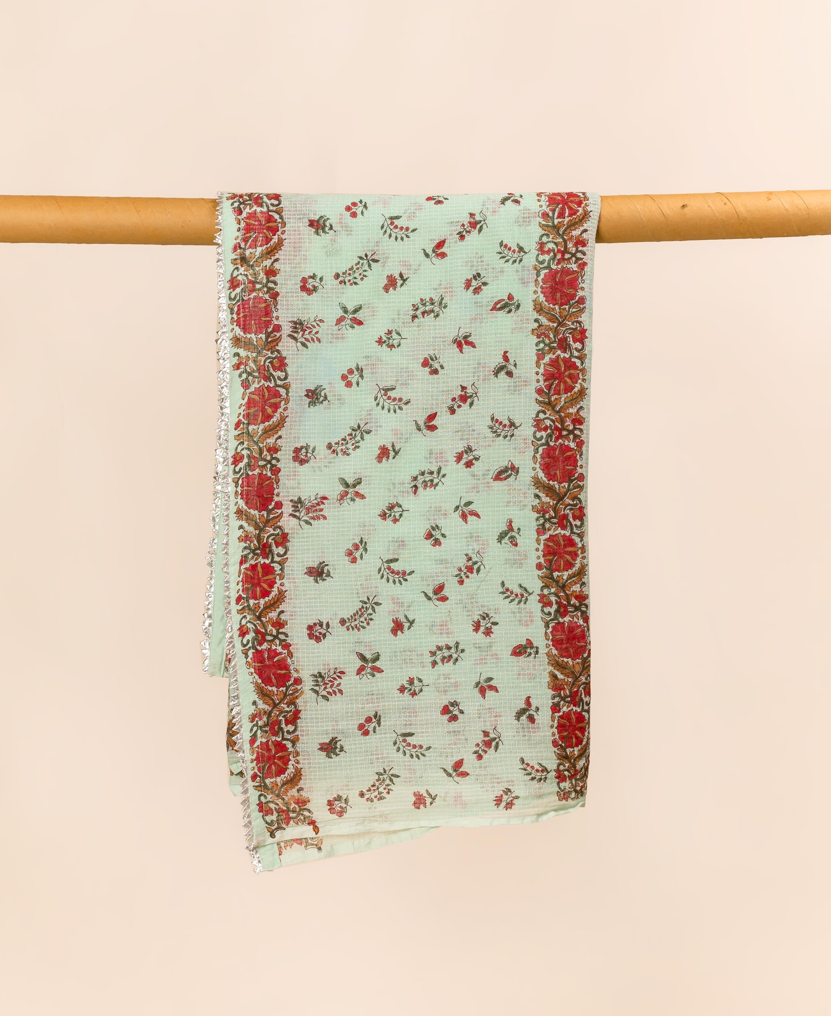 Mint green hand block printed dupatta with red floral designs and silver trim, draped on a rod.