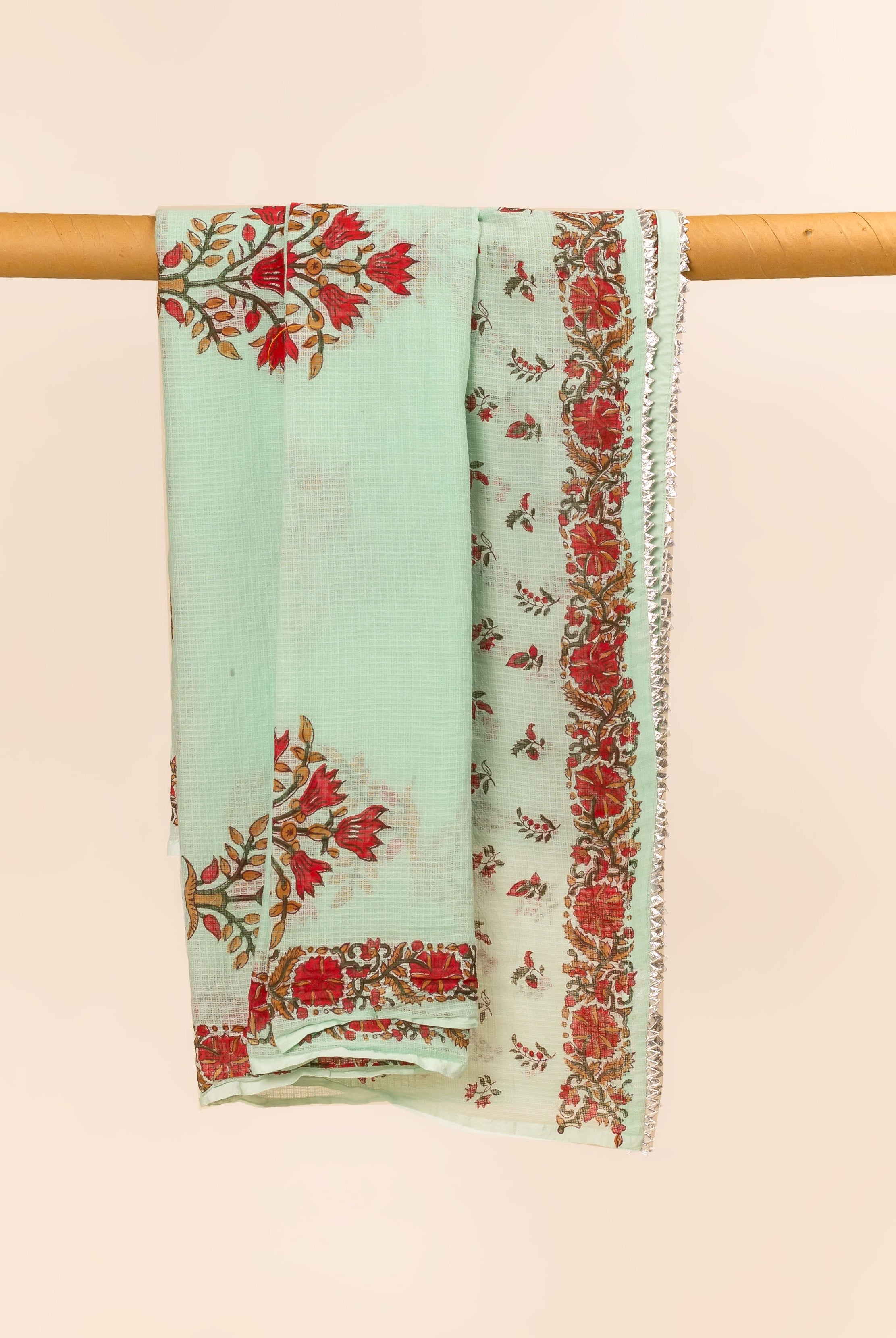 Mint green hand block printed dupatta, featuring red floral patterns and a silver-edged border, hanging.