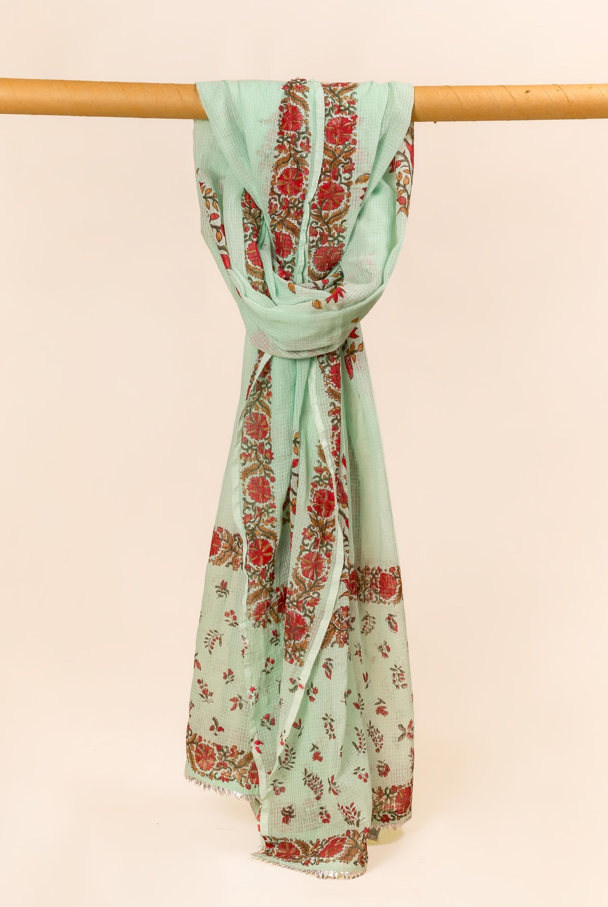 Mint green hand block printed dupatta with red floral patterns, gracefully draped on a wooden bar.