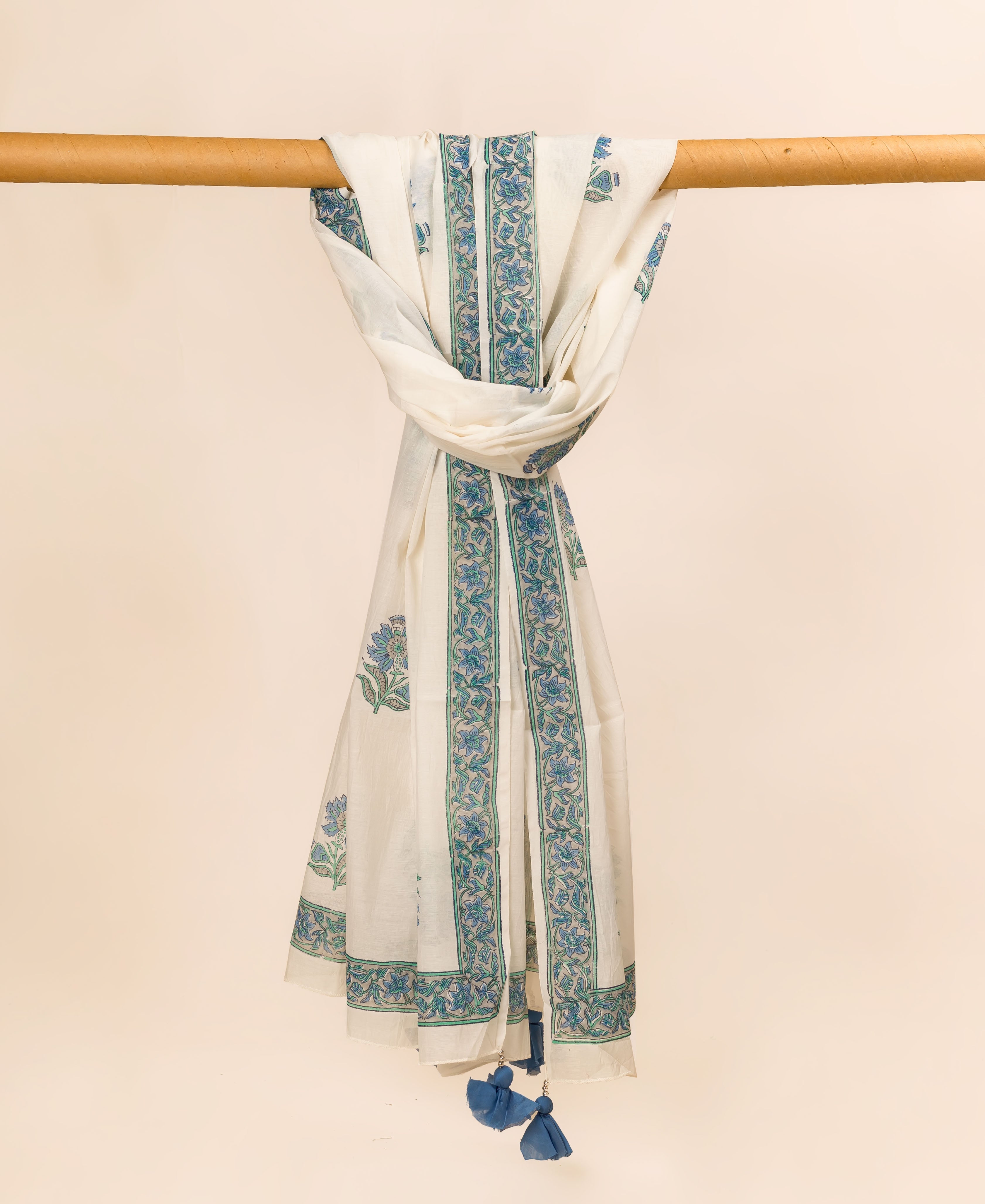 White hand-block printed dupatta draped on a rod with blue-green floral patterns and tassels.