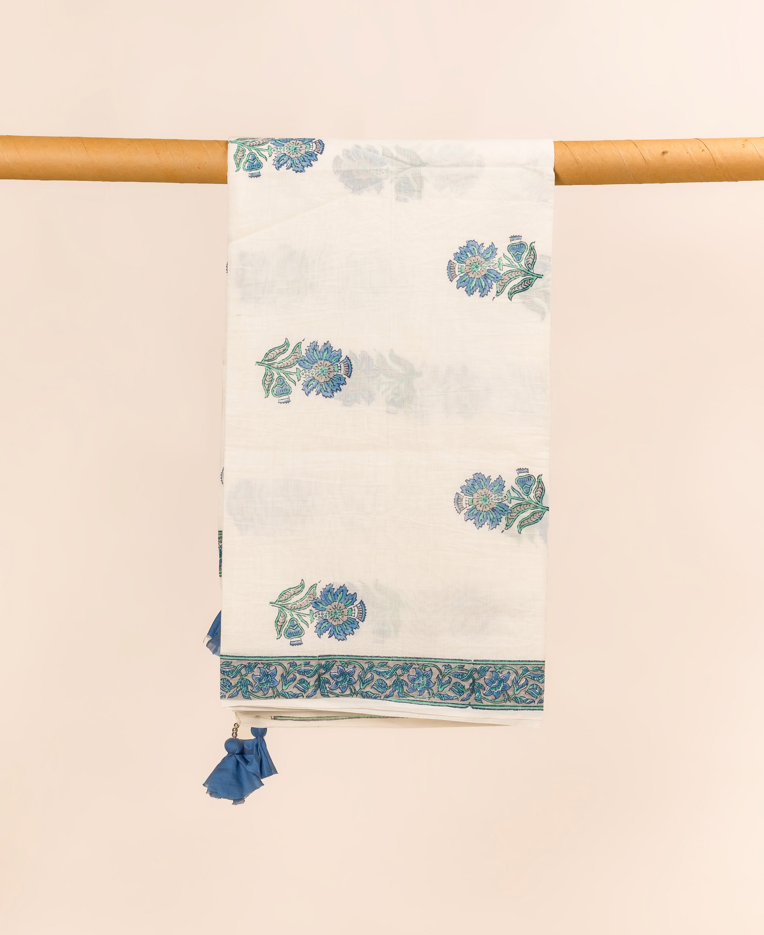 White dupatta with blue and green hand block printed florals, a border, and tassels, hanging.