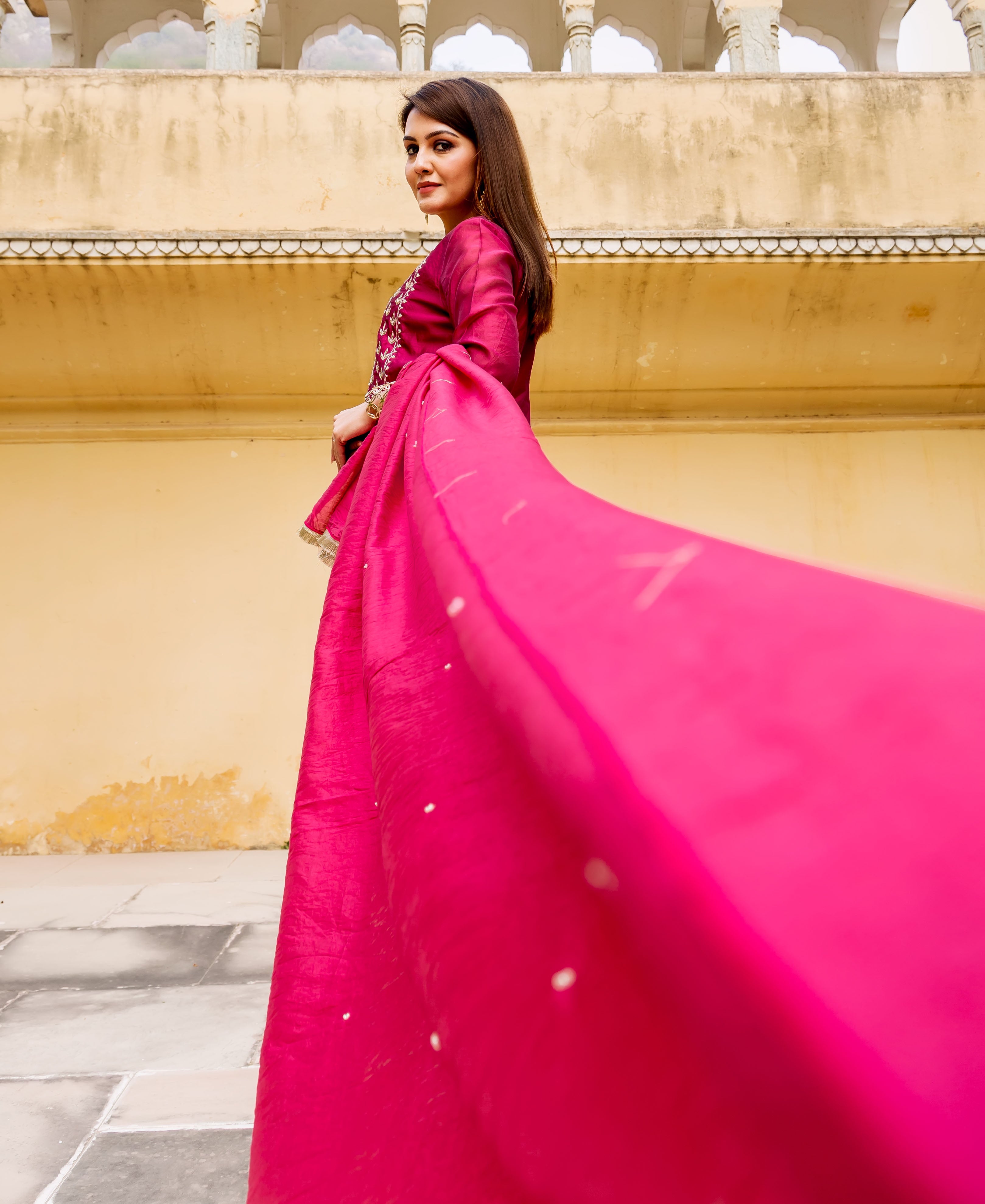 Low angle shot of a model showcasing a vibrant pink flowing dupatta with scattered beads.