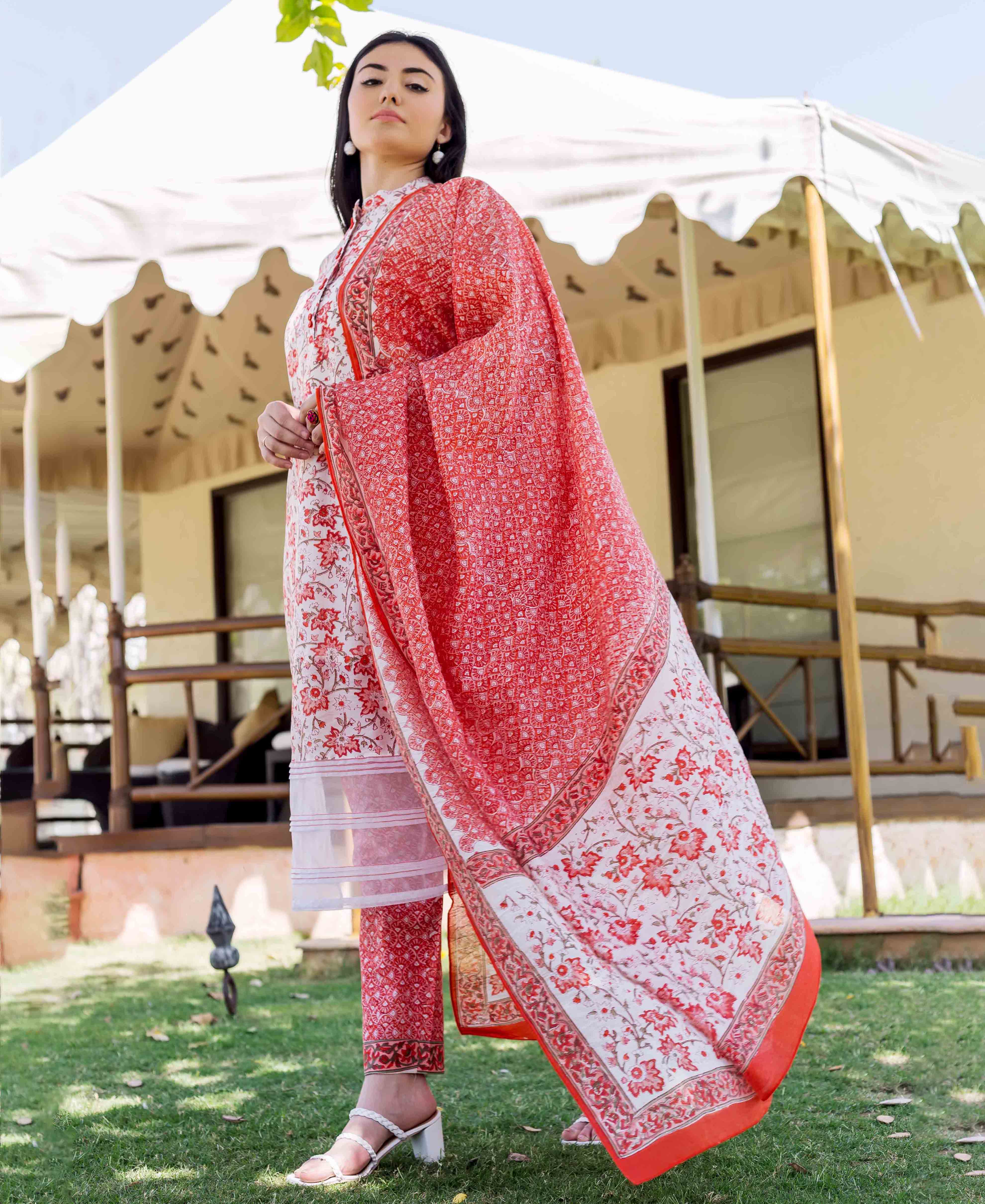 Model wears peach and orange block-printed dupatta flowing over matching suit outdoors.
