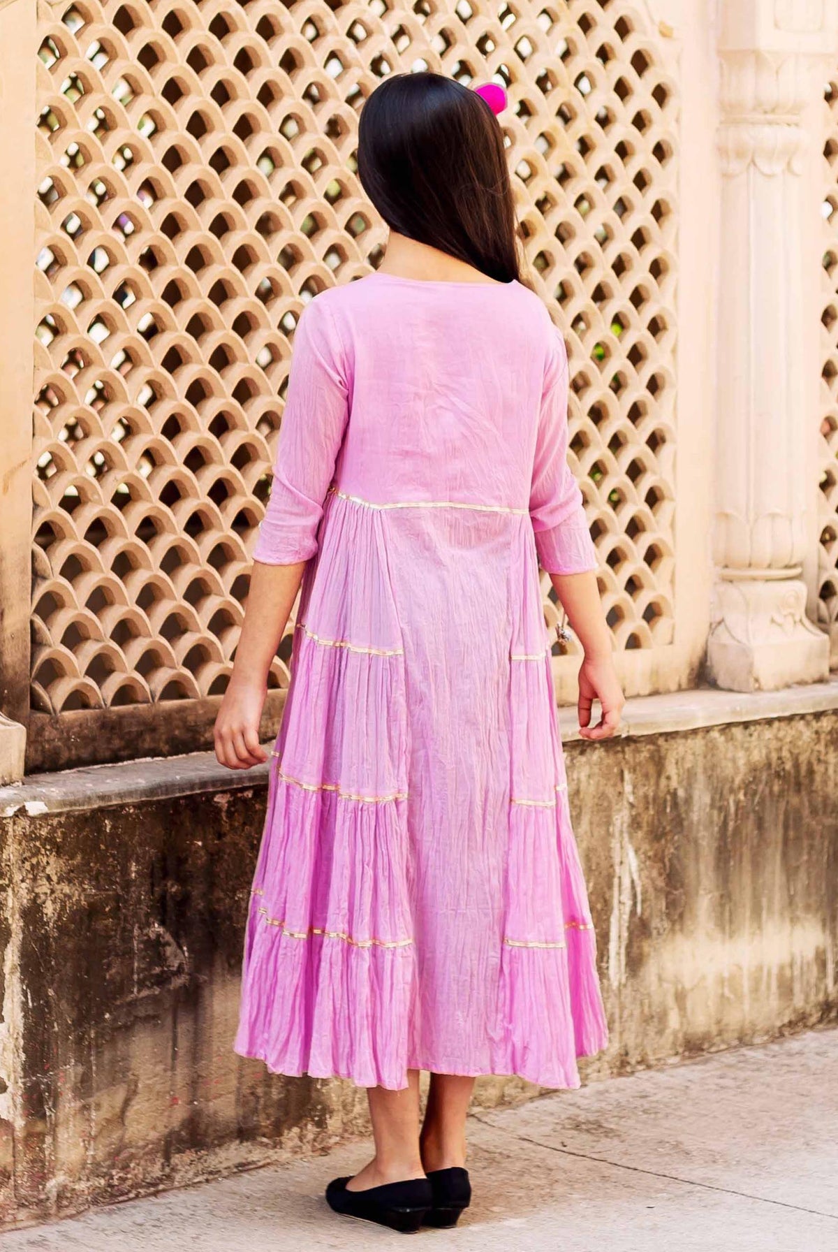 Rear view of a girl wearing a long pink tiered frill dress with golden gota.