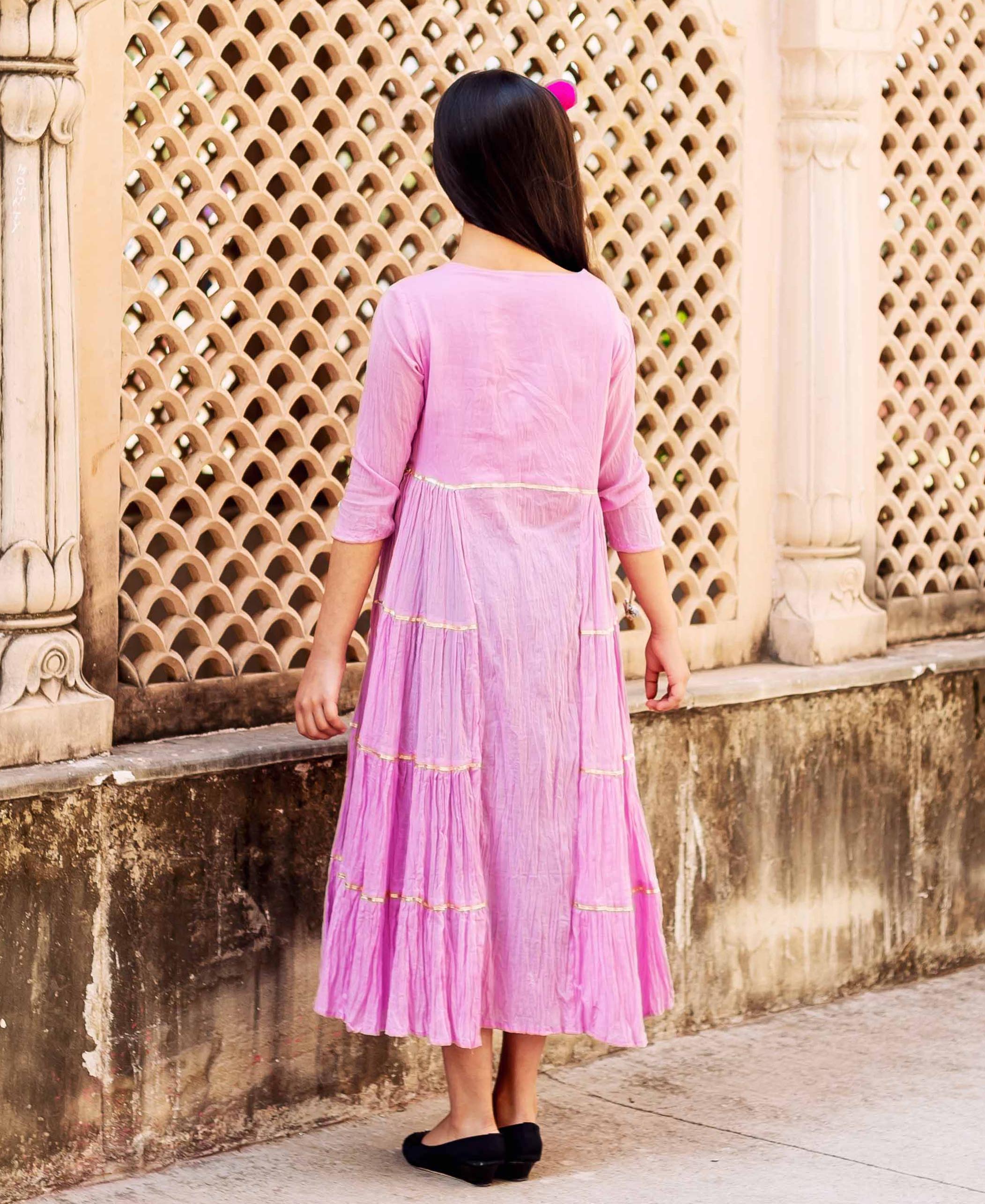 Rear view of a girl wearing a long pink tiered frill dress with golden gota.