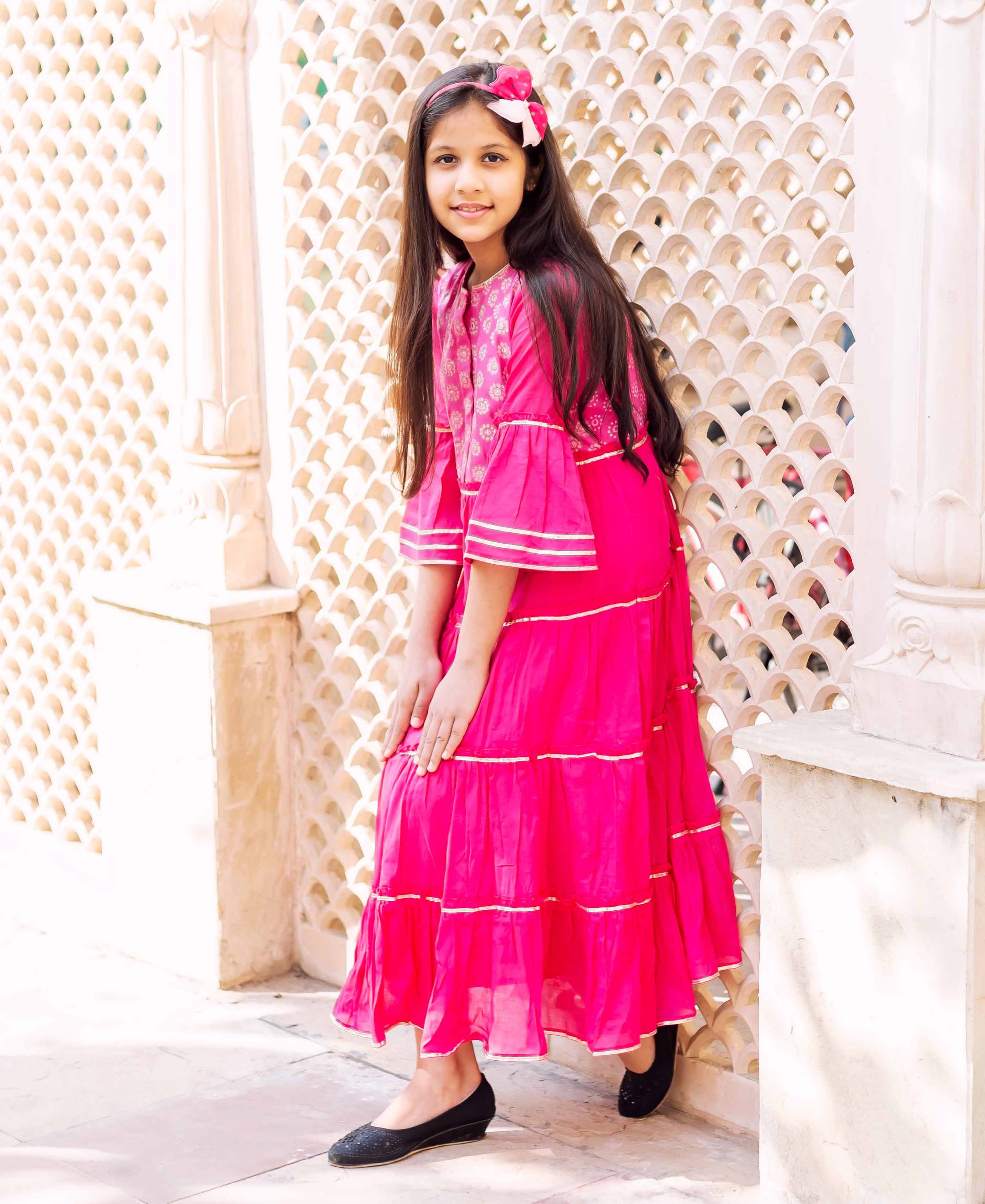 Front view of young girl wearing fuchsia tiered long ethnic dress with gold gota trim.
