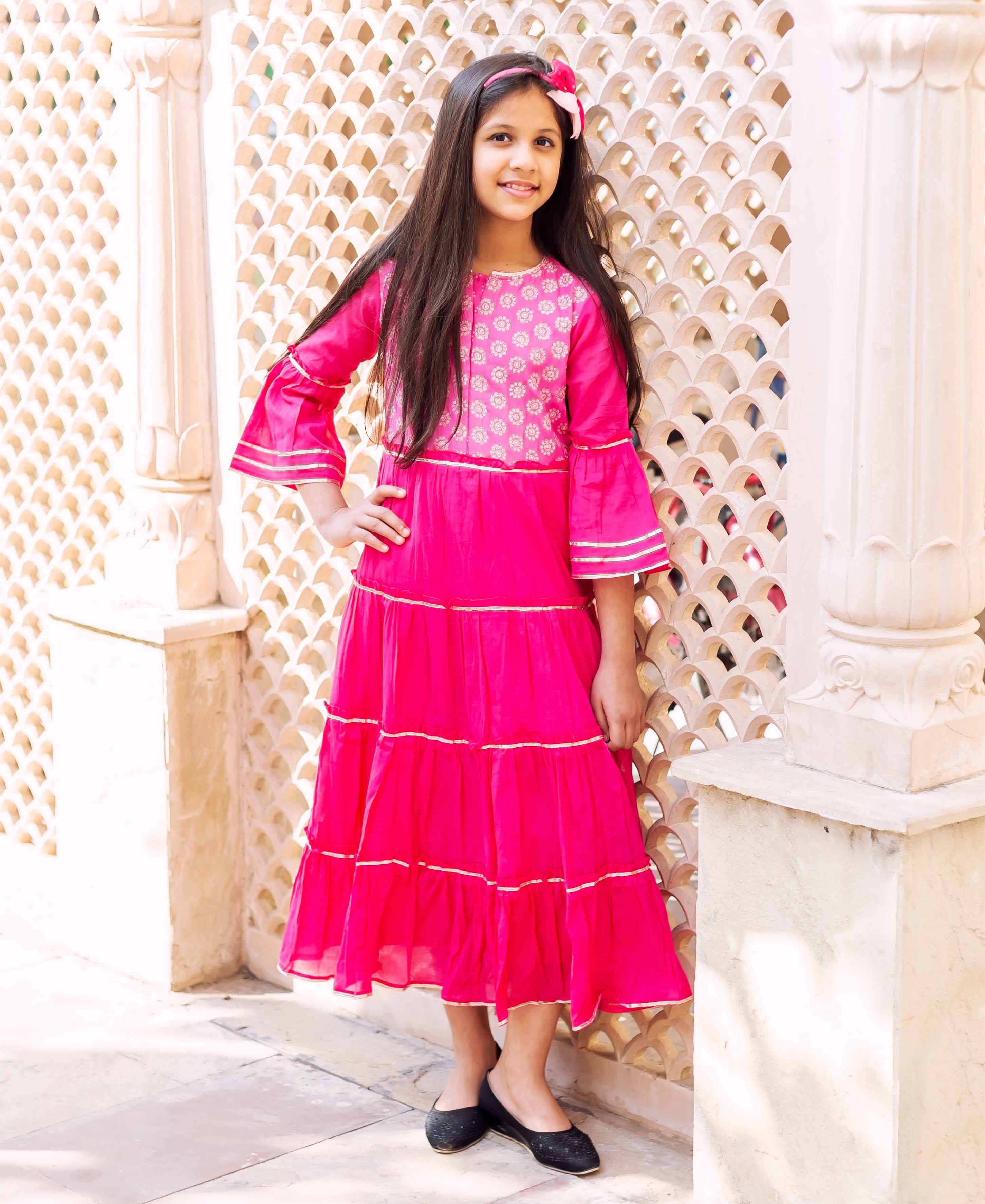 Fuchsia long tiered dress, white block print yoke, flared sleeves, golden trim on girl.