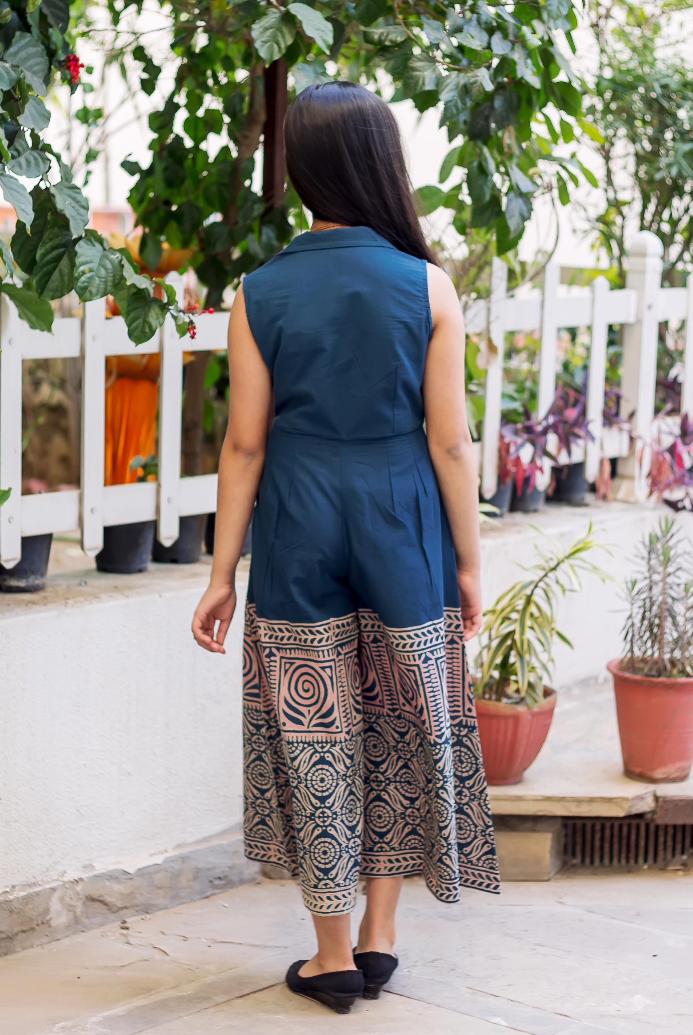 A model wearing a blue and white hand-block-printed jumpsuit, facing away from the camera.