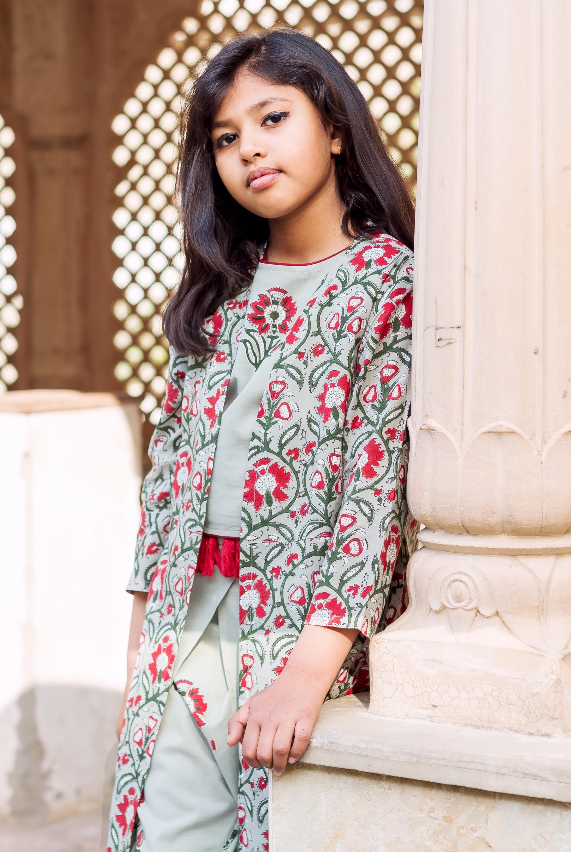 Young girl wearing frosty mint block printed crop top, dhoti, and jacket with red and green florals.