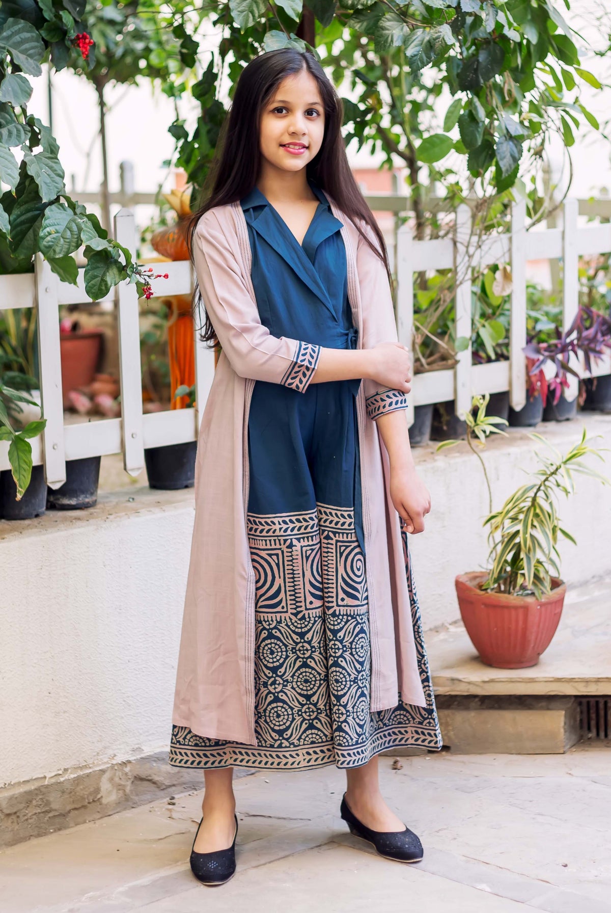 Young girl in an indigo blue block printed jumpsuit with a long pink jacket.