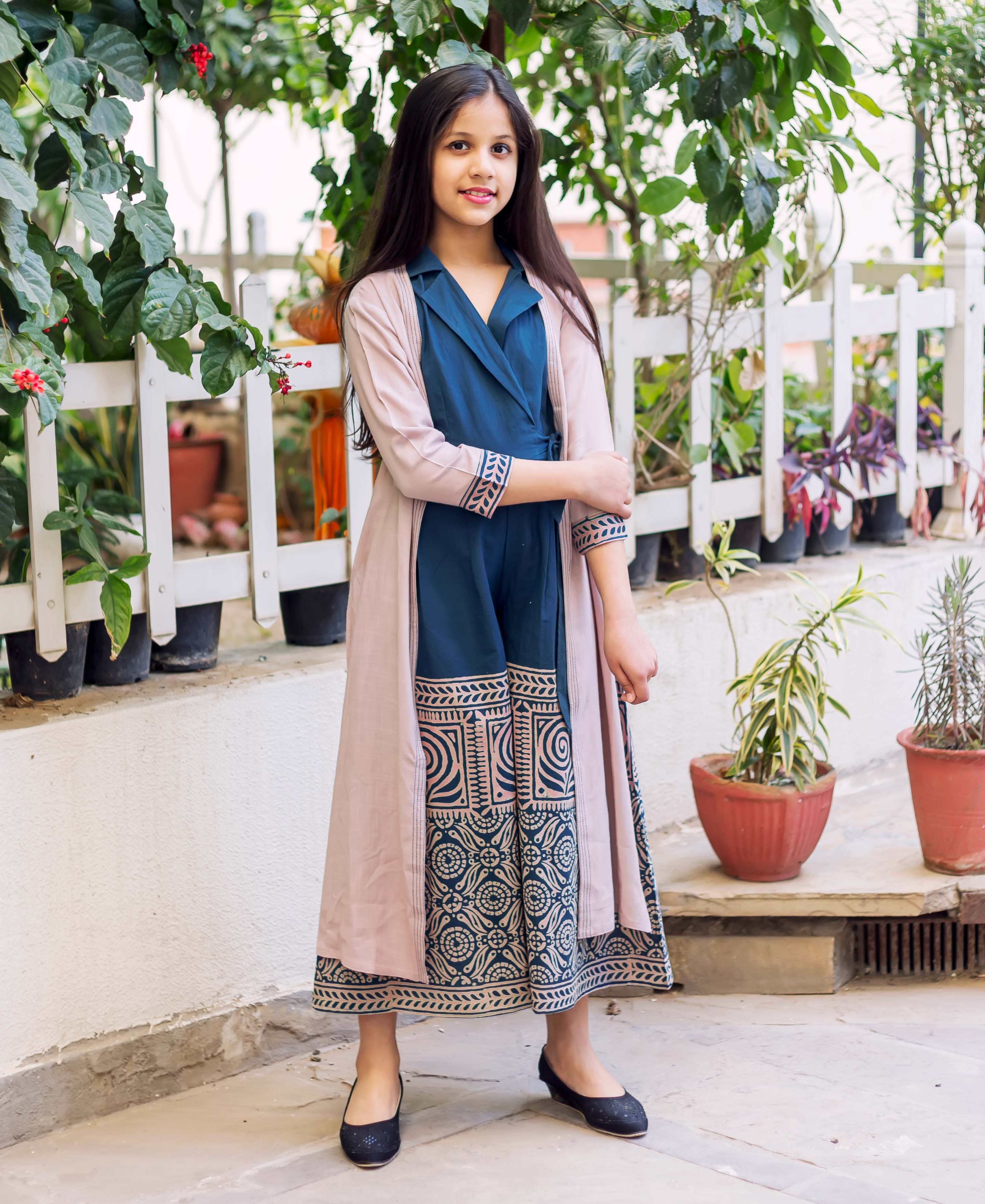 Young girl in an indigo blue block printed jumpsuit with a long pink jacket.