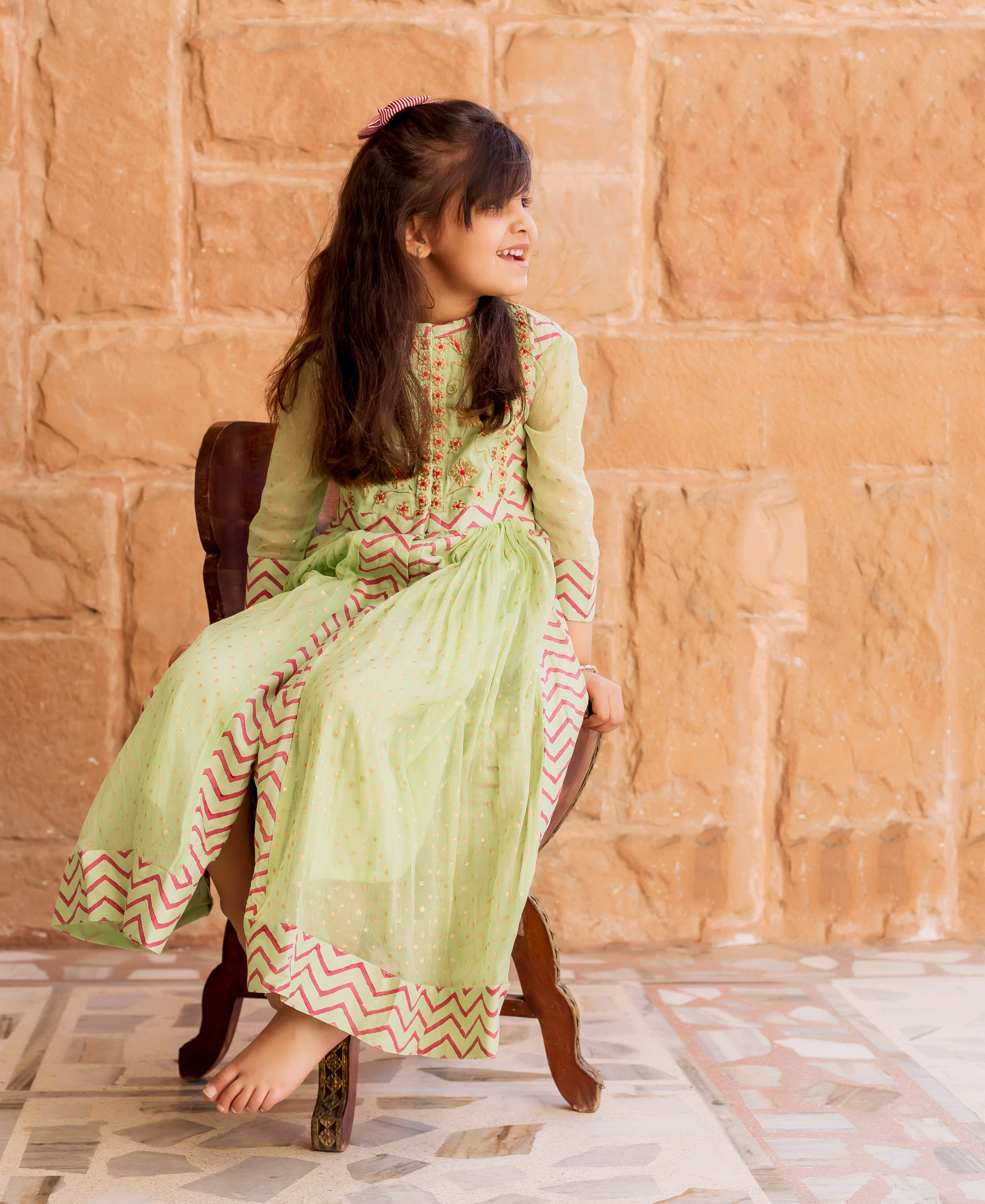 Baby girl wears a flowing mint green chiffon Anarkali dress with red block prints.