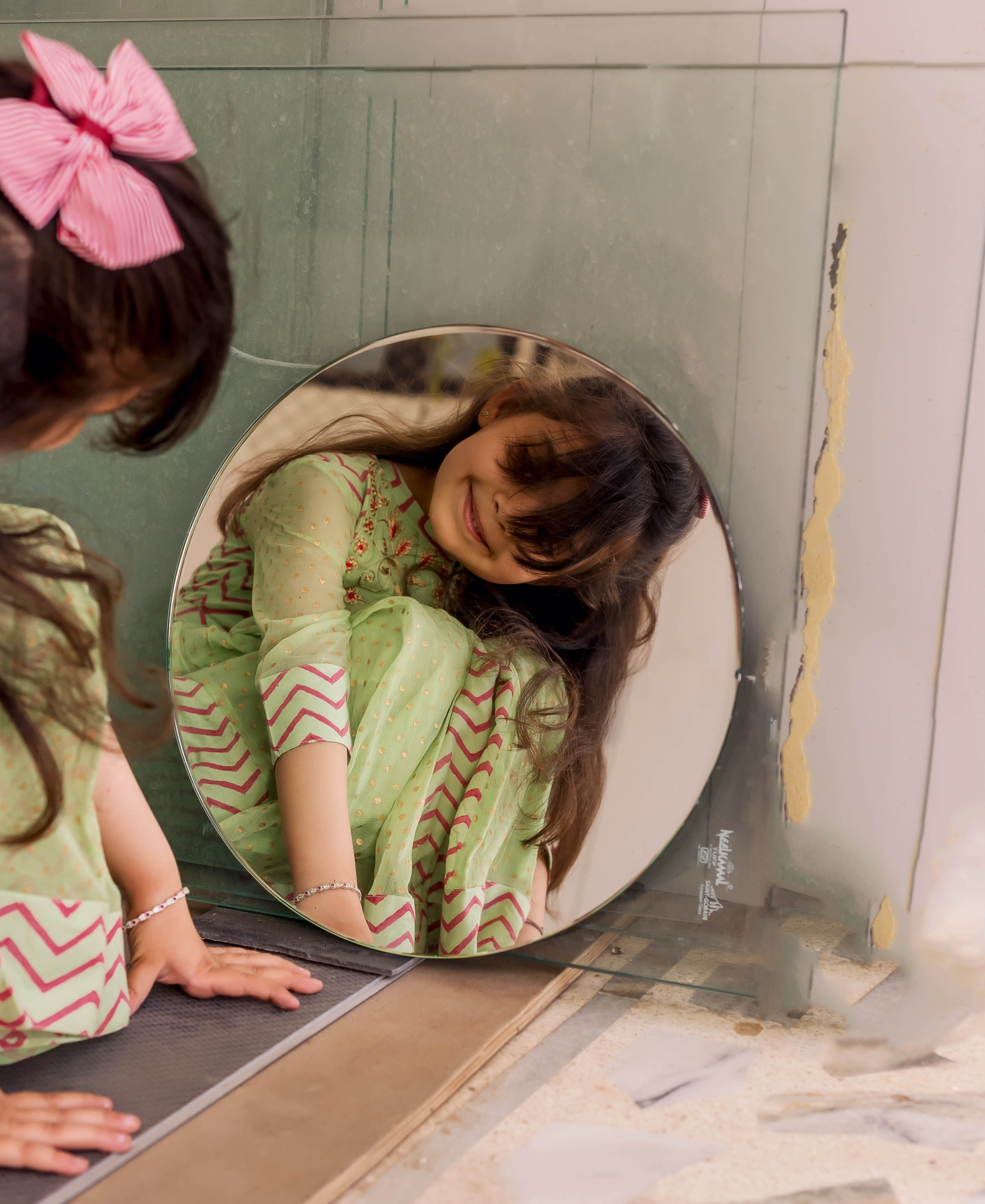 Smiling girl reflected in mirror wearing a mint green dress with polka dot and chevron prints.