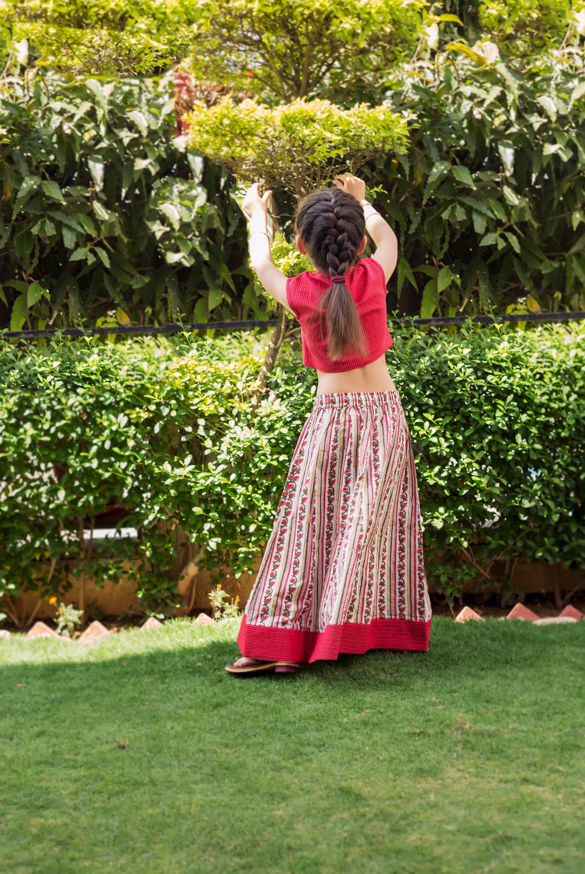 Rear view of a girl wearing a red crop top and white block-printed ethnic skirt.