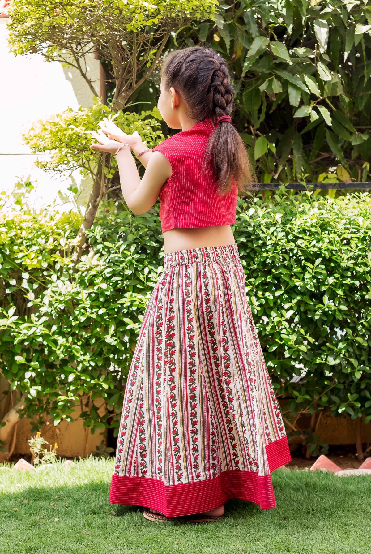 Girl from behind in a red crop top and block-printed white, red, and green floral striped skirt.
