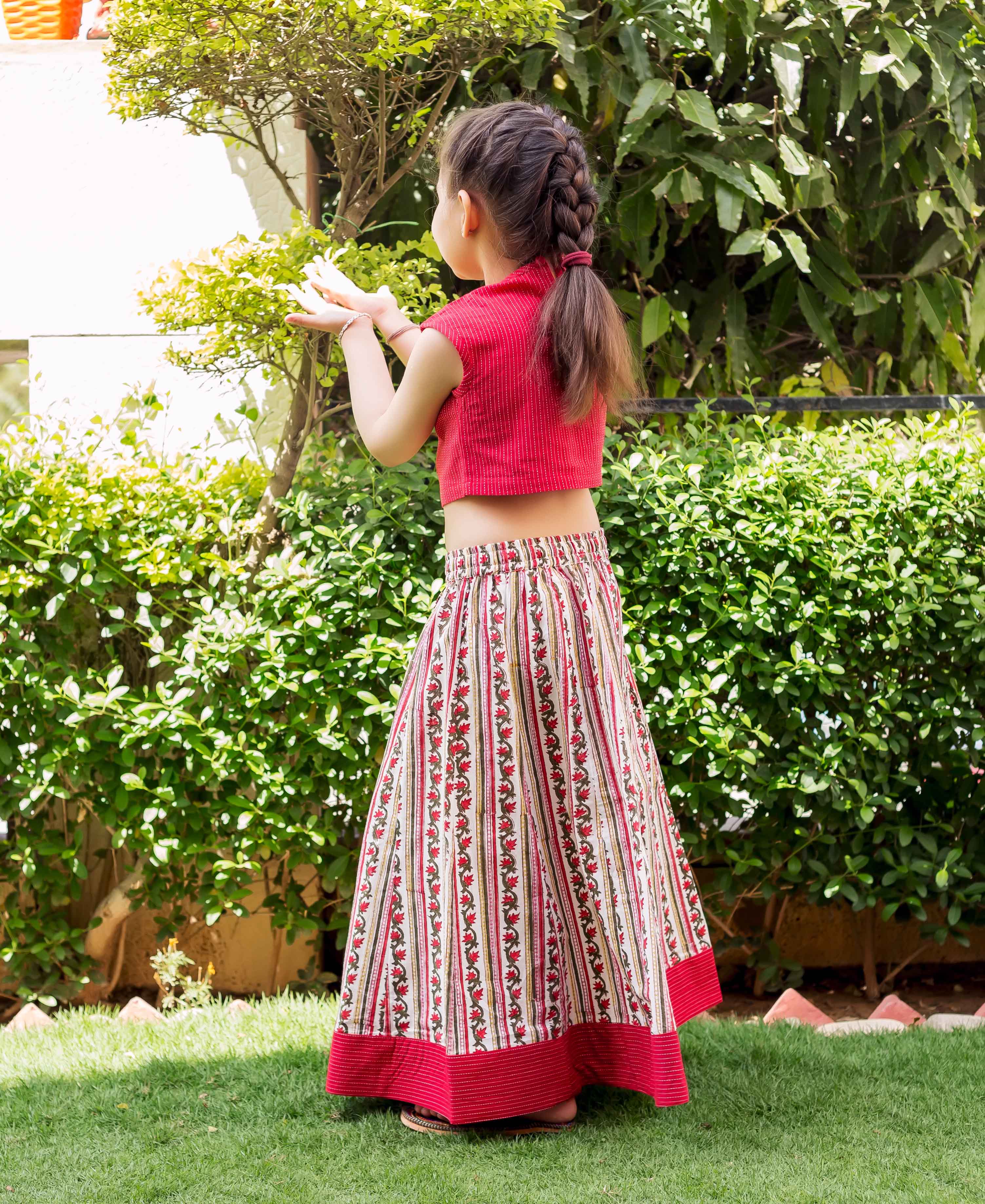 Girl from behind in a red crop top and block-printed white, red, and green floral striped skirt.