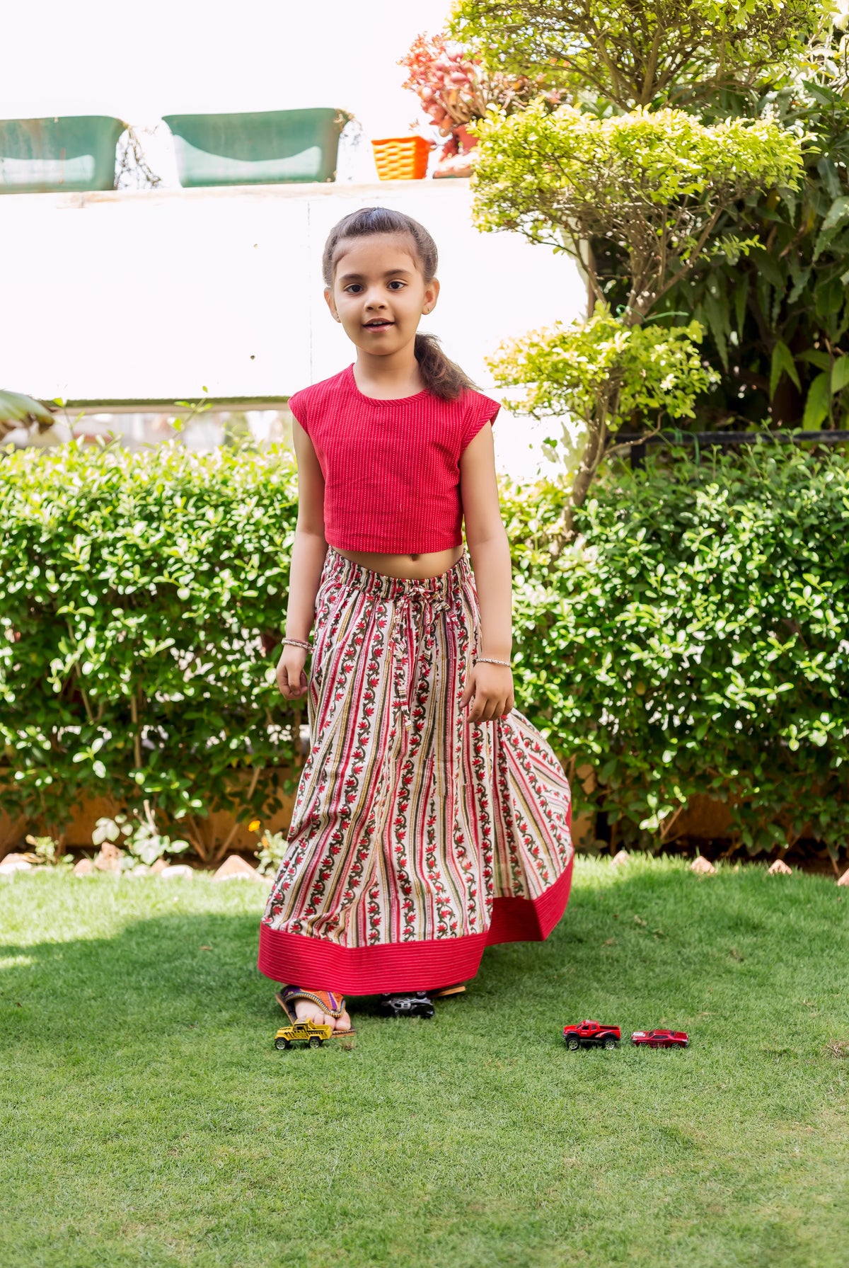 Young girl in a red sleeveless crop top and white floral block printed ethnic skirt.