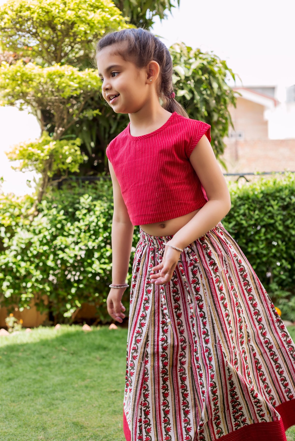 Young girl models red textured crop top and block printed floral skirt with red accents.