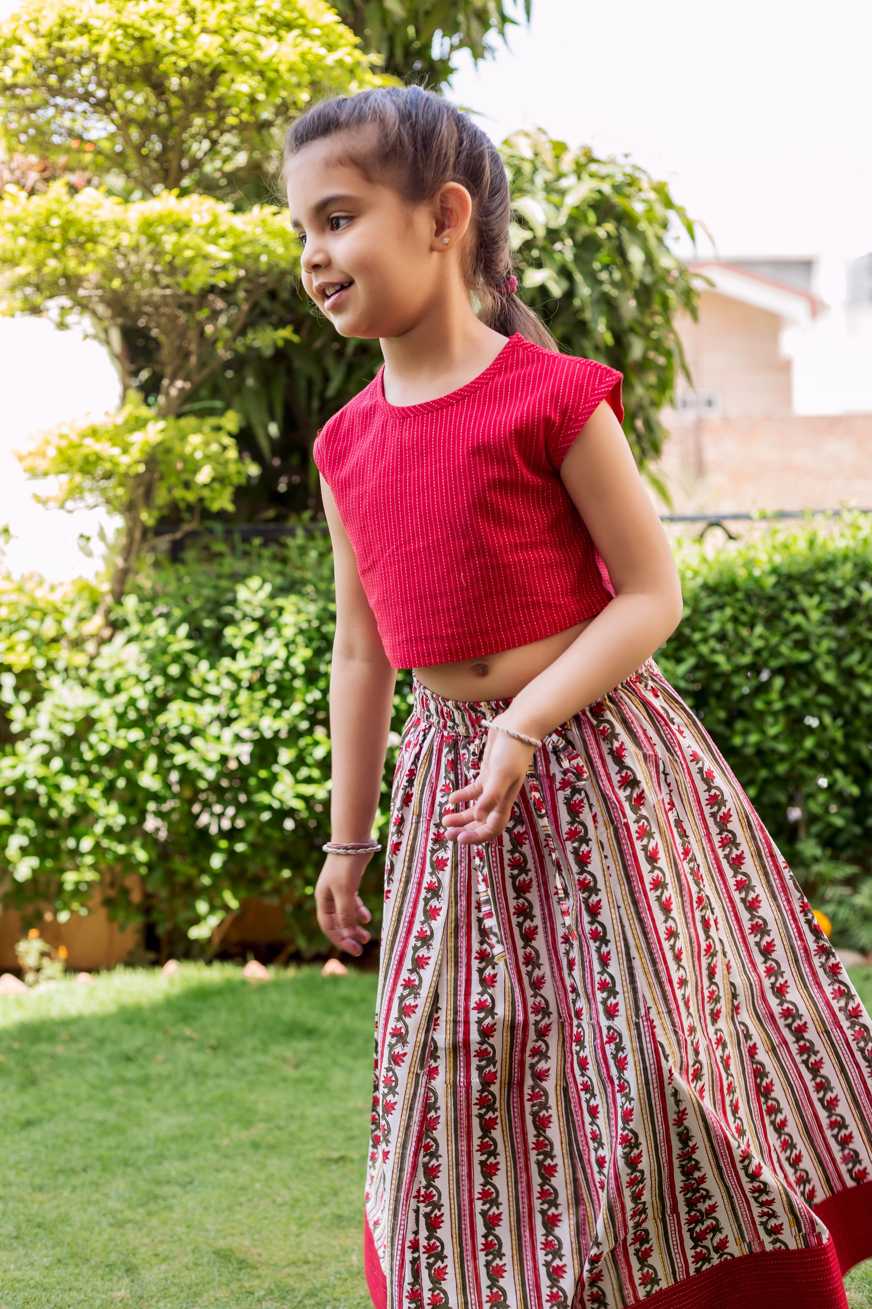 Young girl models red textured crop top and block printed floral skirt with red accents.