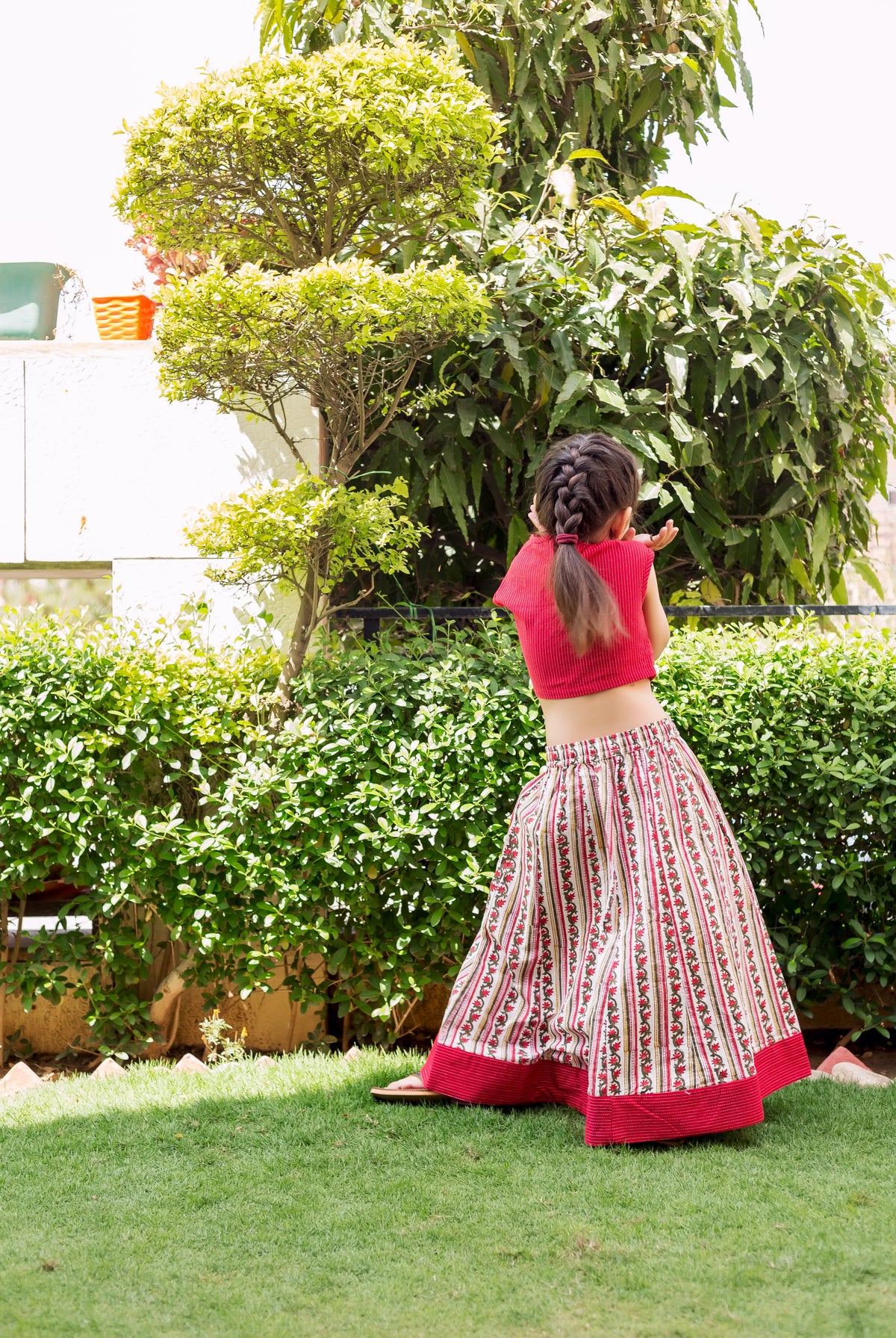 Child from back in red crop top and white striped, block-printed ethnic skirt.