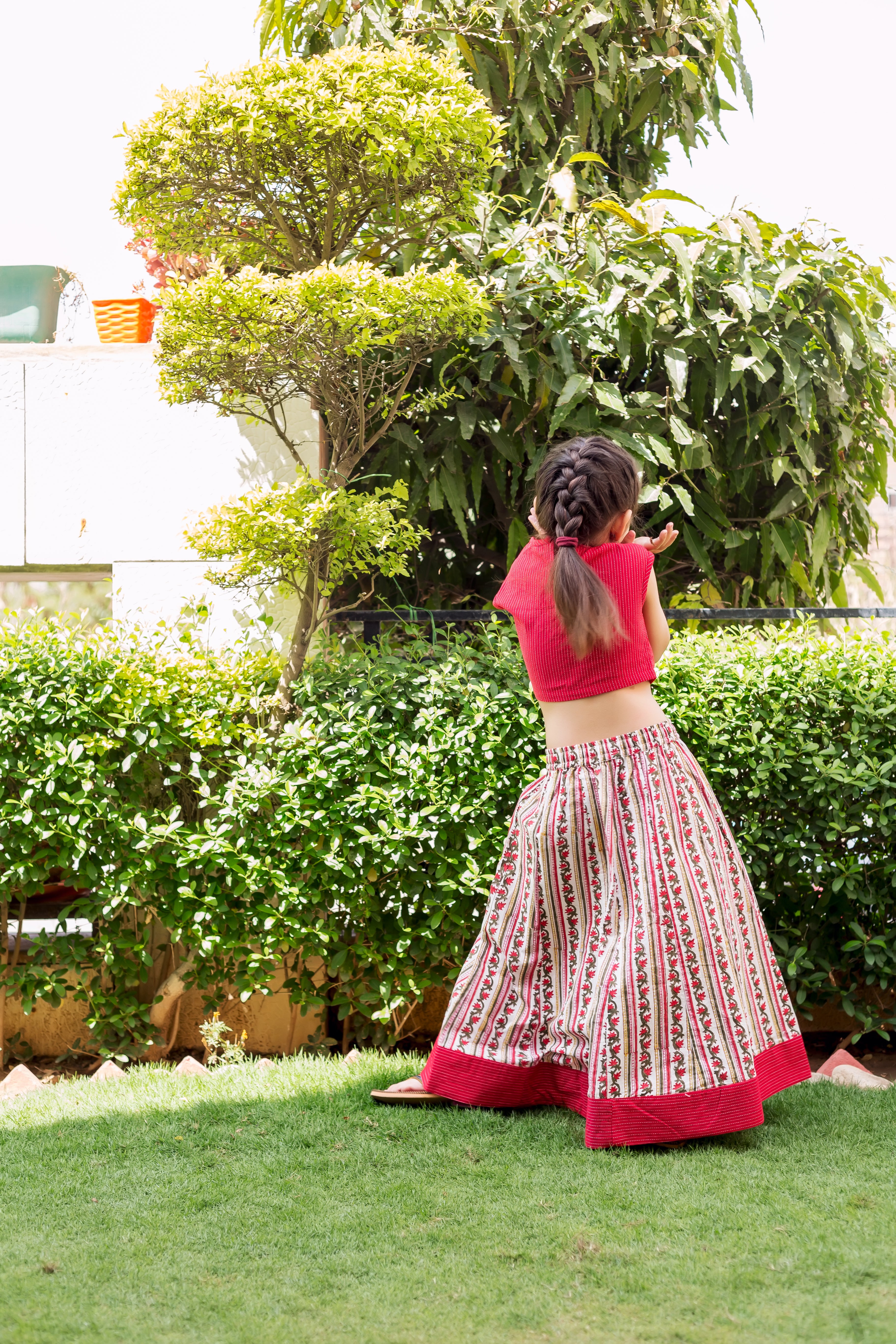 Child from back in red crop top and white striped, block-printed ethnic skirt.