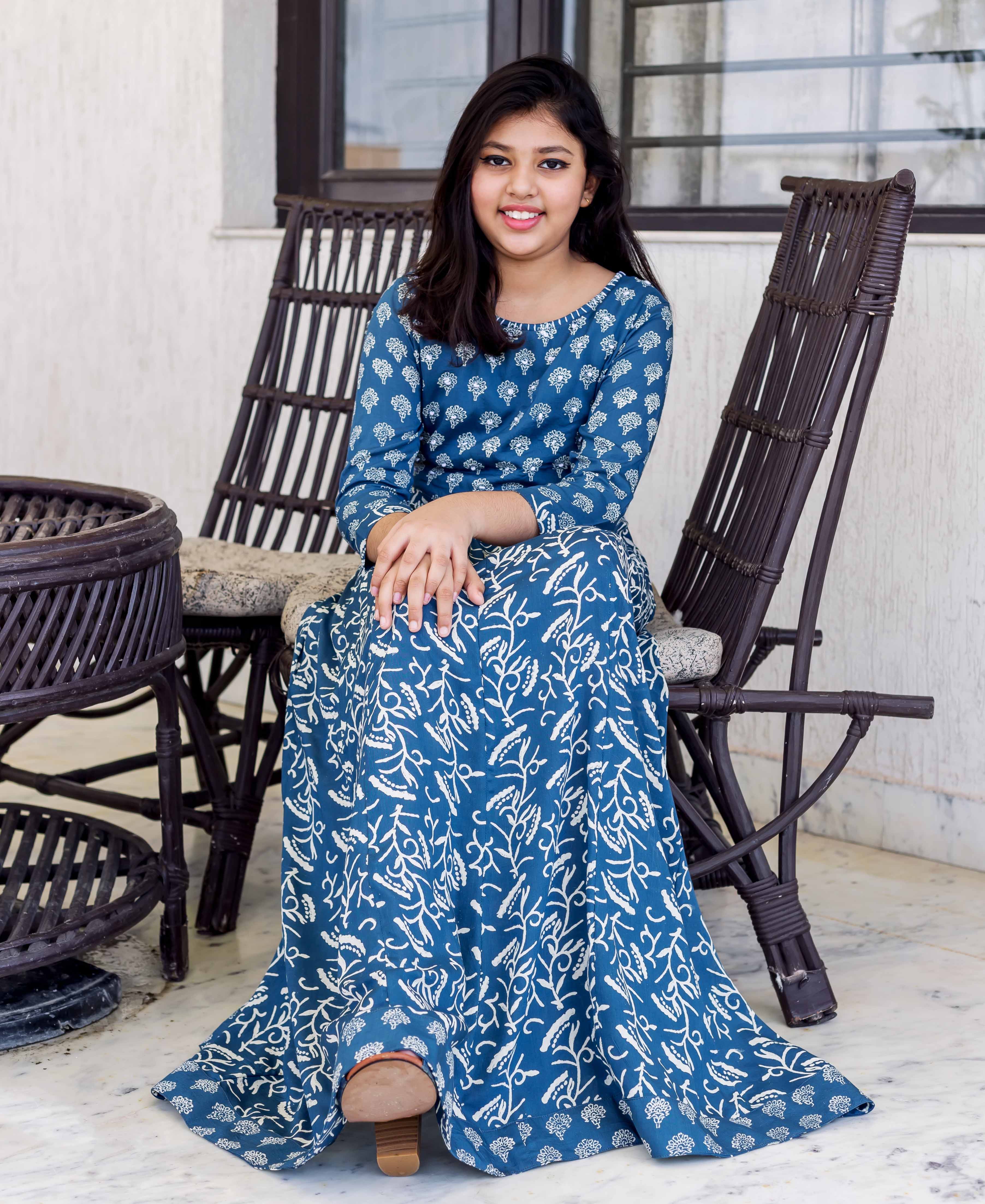 Indigo printed long dress with white floral patterns on a young girl sitting outdoors.