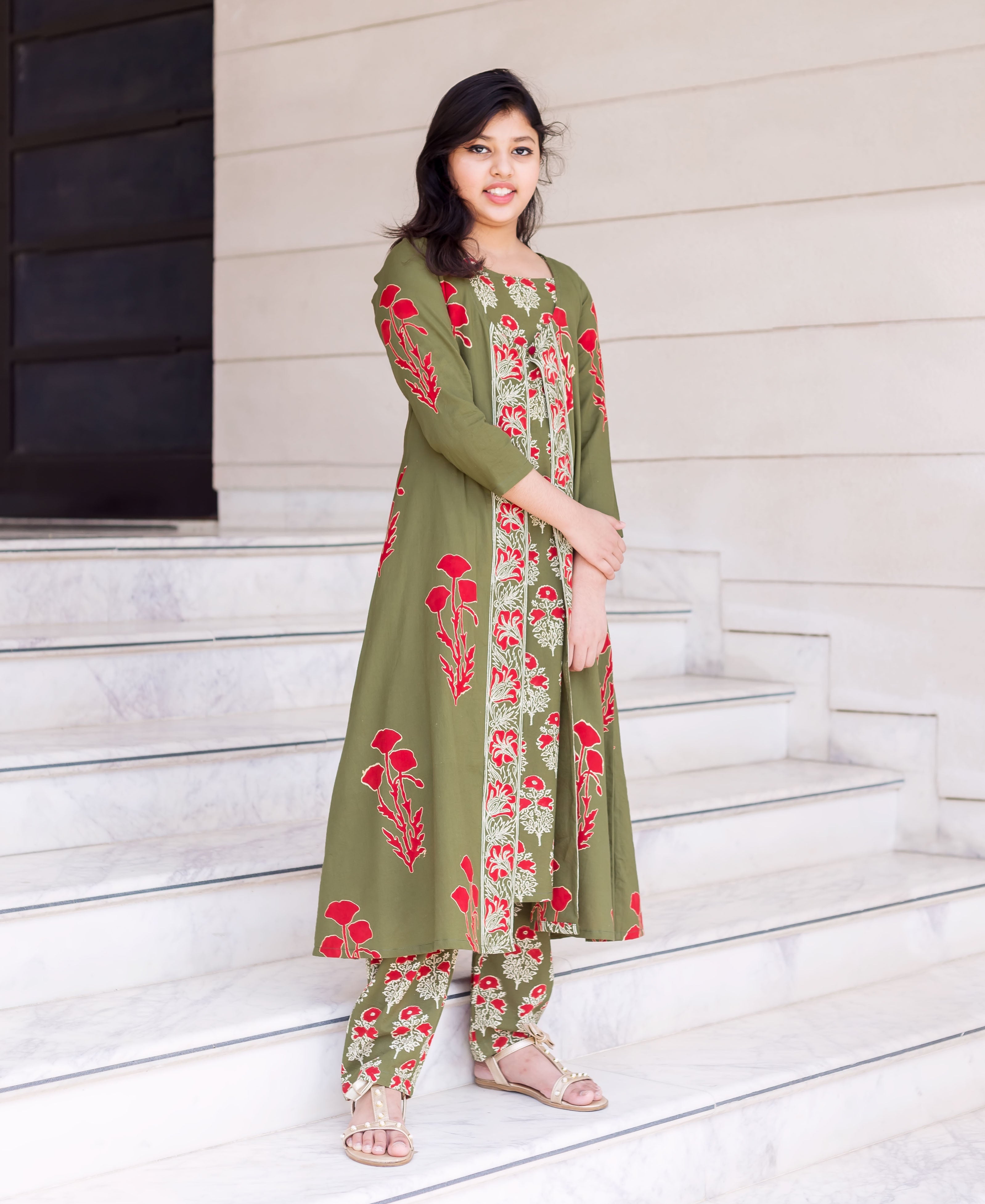 Young girl models olive green kurta set with red and cream floral print, standing on stairs.