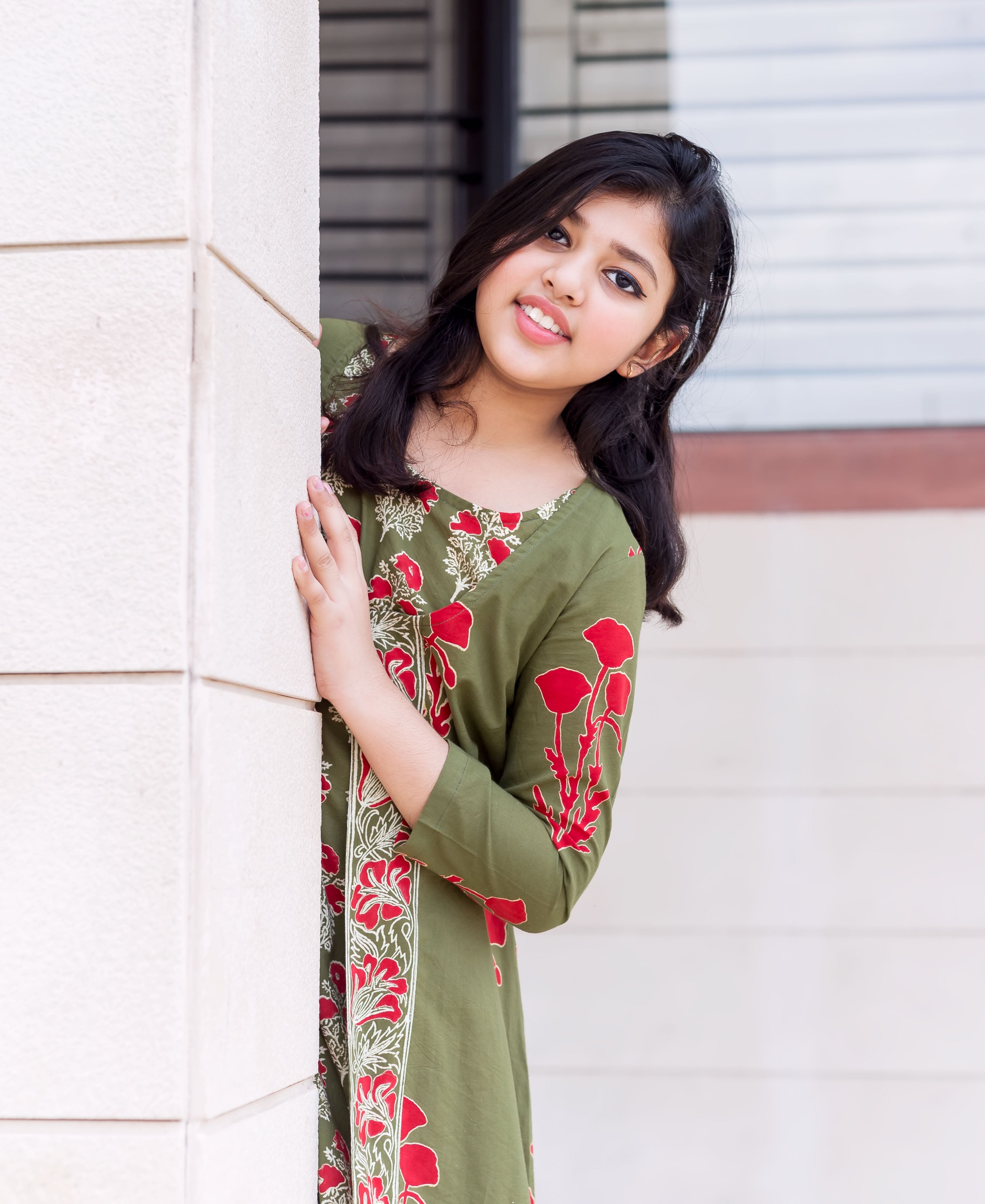 Olive green kurta with bold red hand-block floral print, worn by young girl peeking.