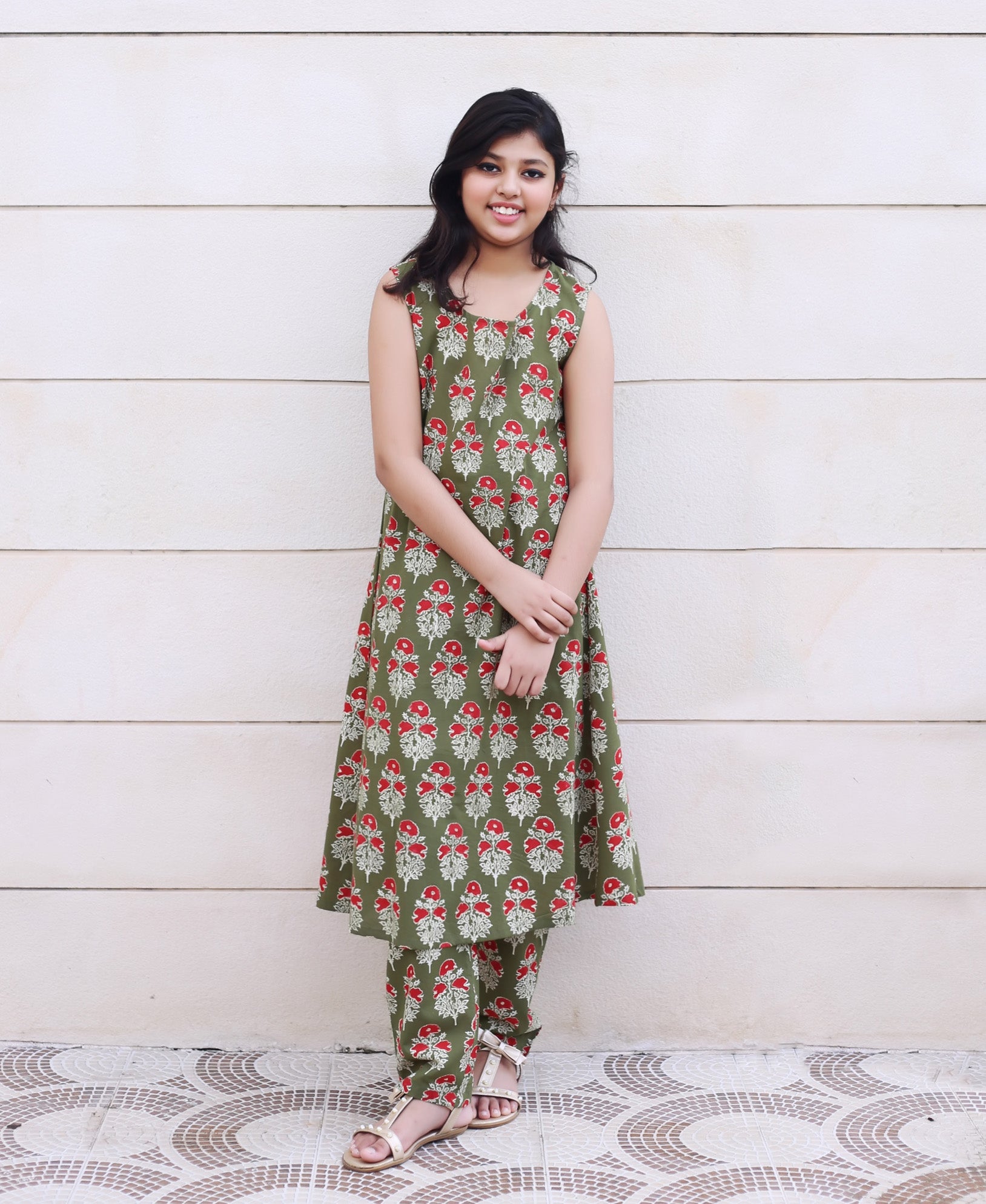 Young girl models olive green sleeveless kurta set with repeating red floral print.