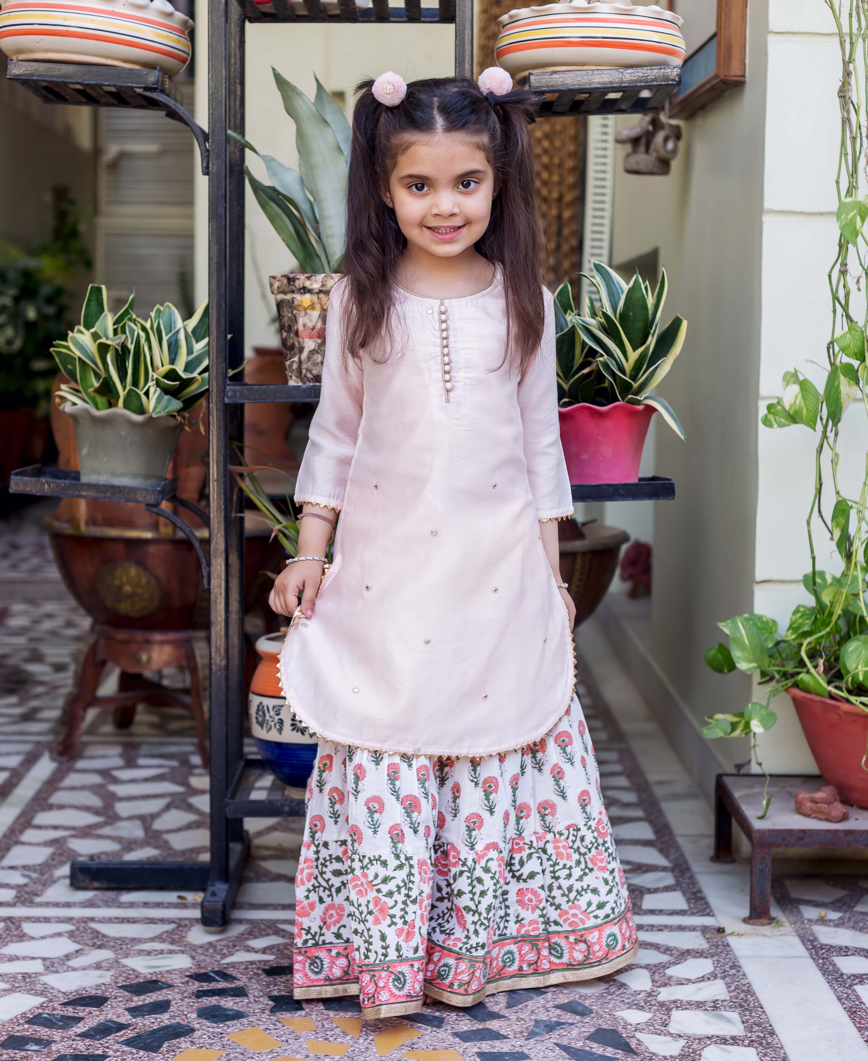 A young girl wearing a pink embroidered kurta and floral sharara.