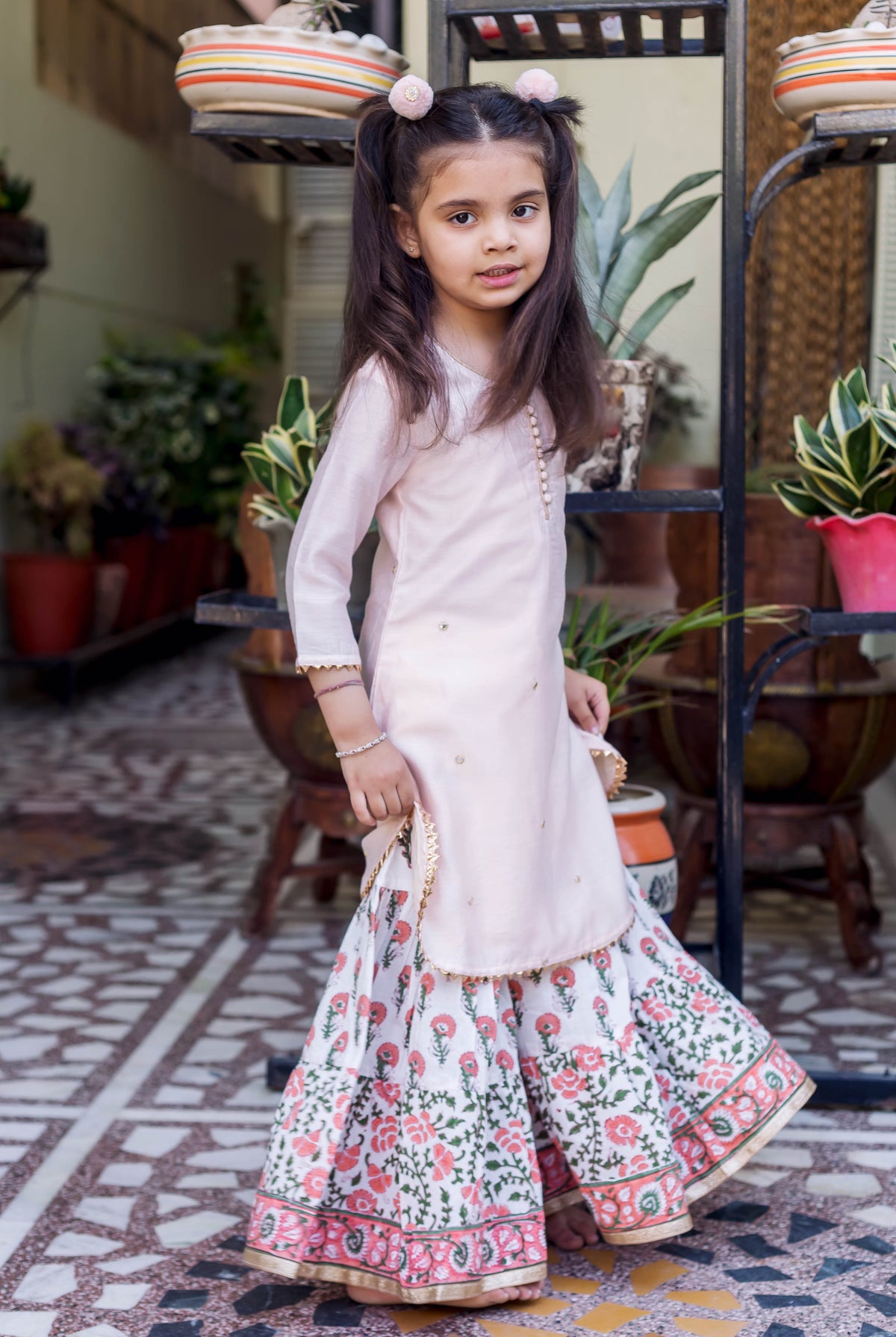 Young girl wearing a light pink embroidered short kurta and white floral printed sharara.