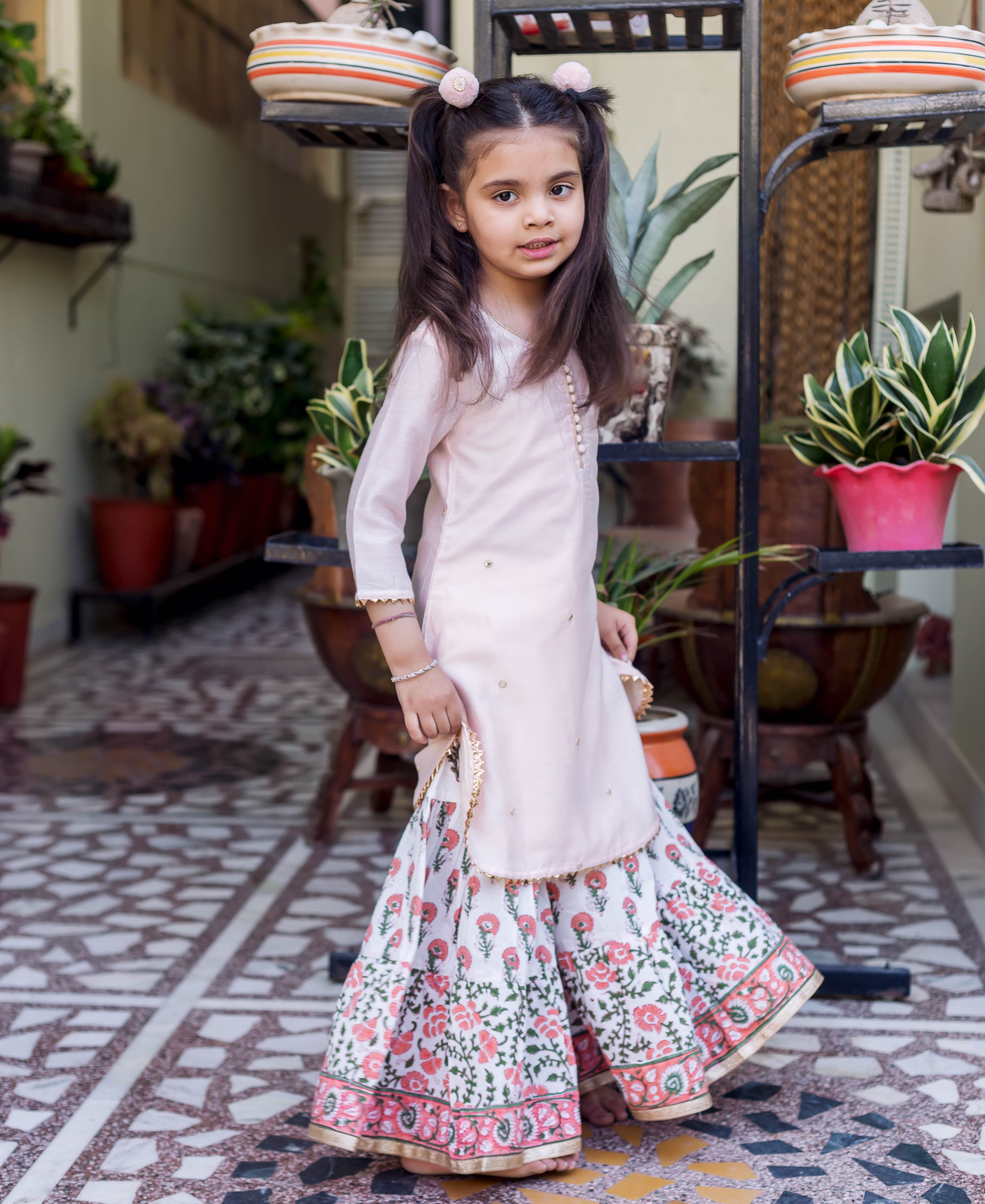 Young girl wearing a light pink embroidered short kurta and white floral printed sharara.