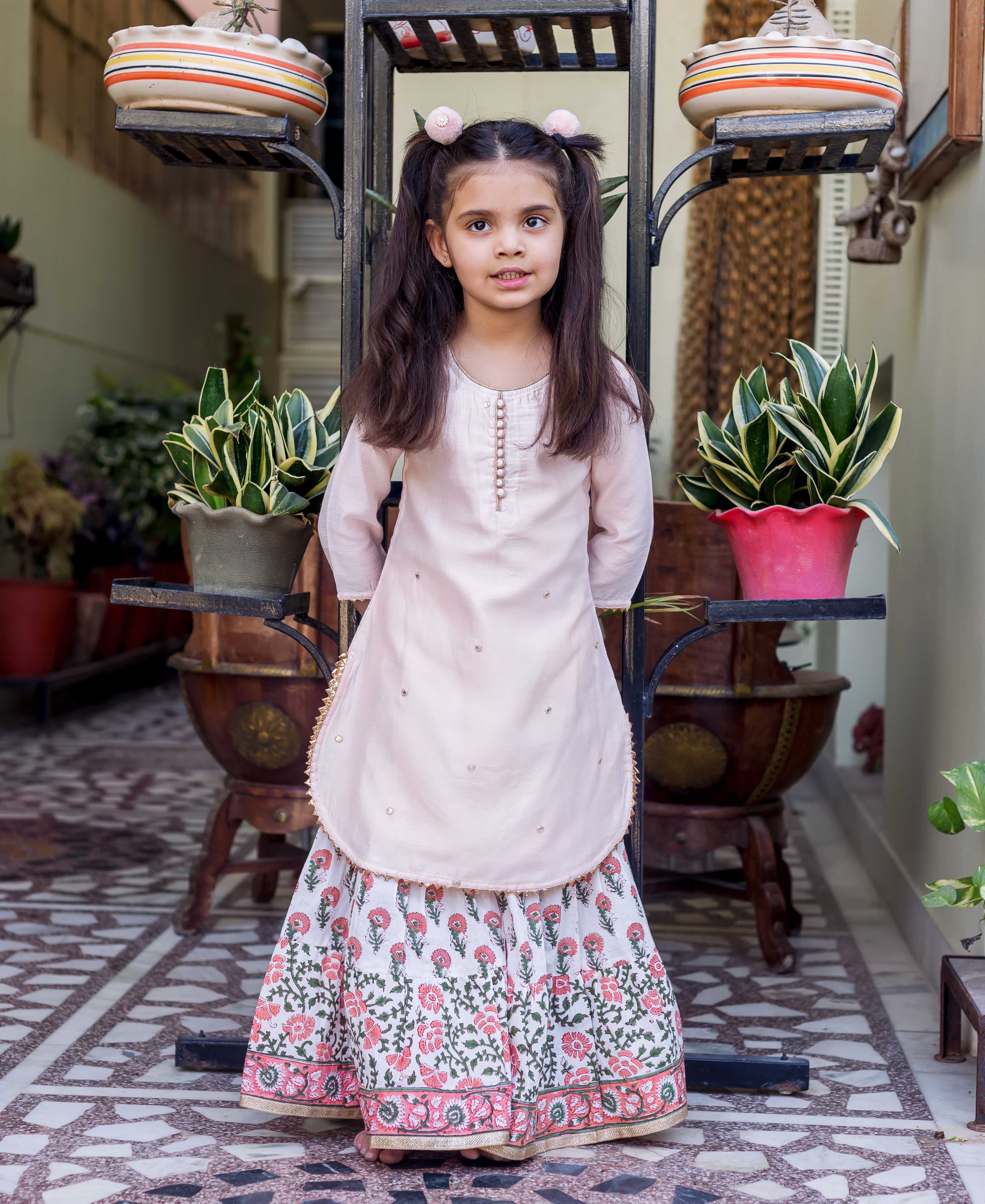 Pink embroidered straight short kurta with white and pink printed sharara on a young girl.