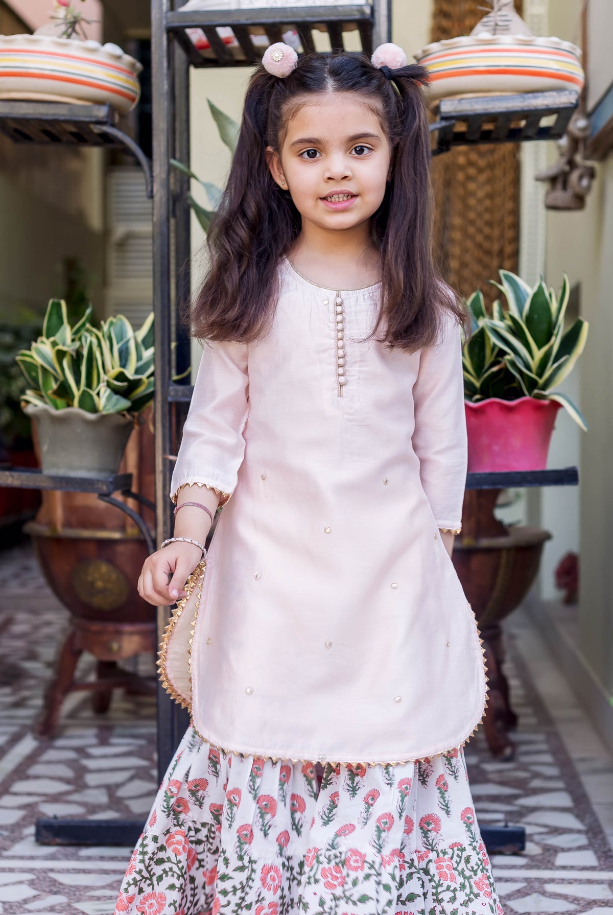 Little girl in light pink embroidered kurta and white floral printed sharara.