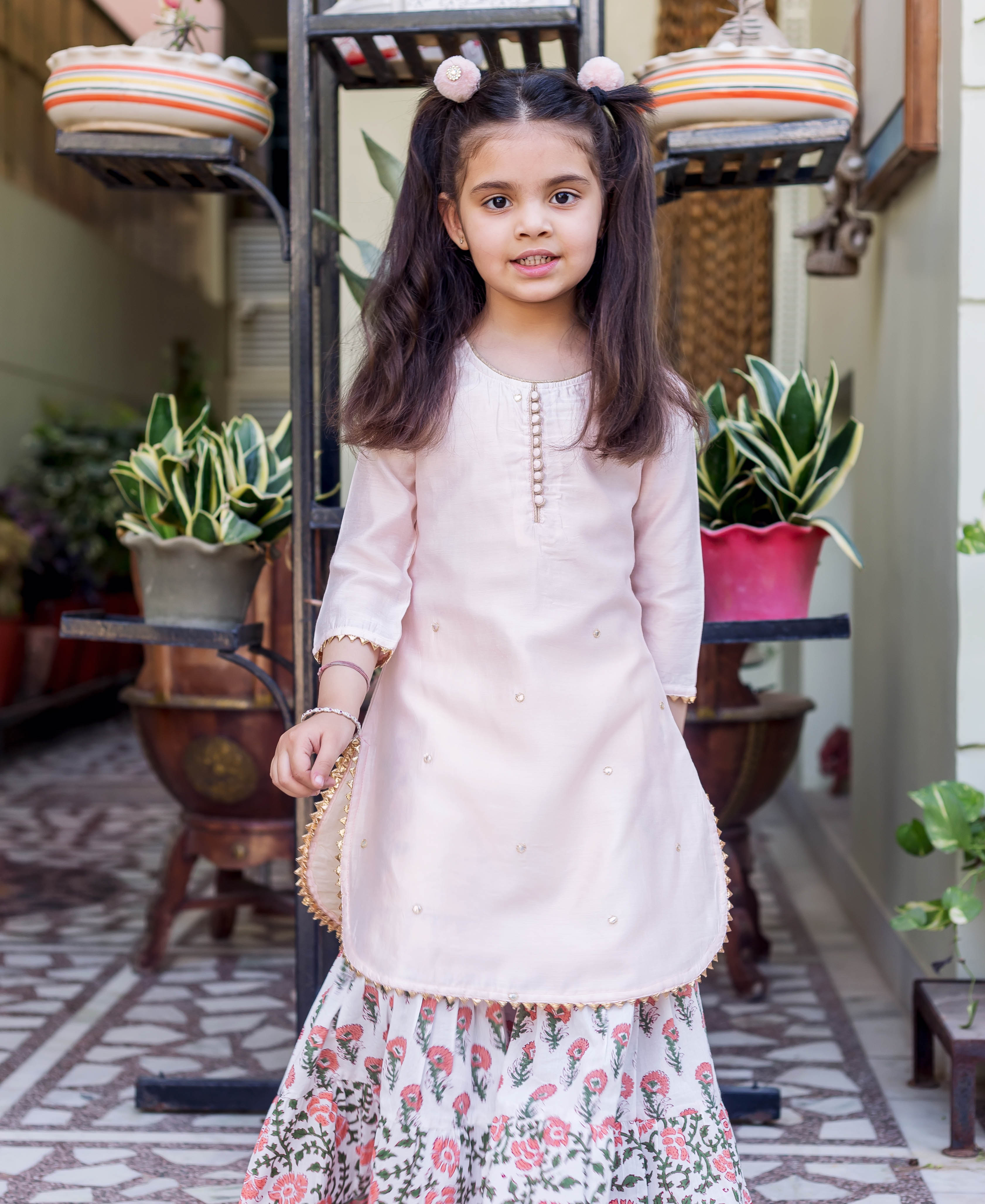 Little girl in light pink embroidered kurta and white floral printed sharara.