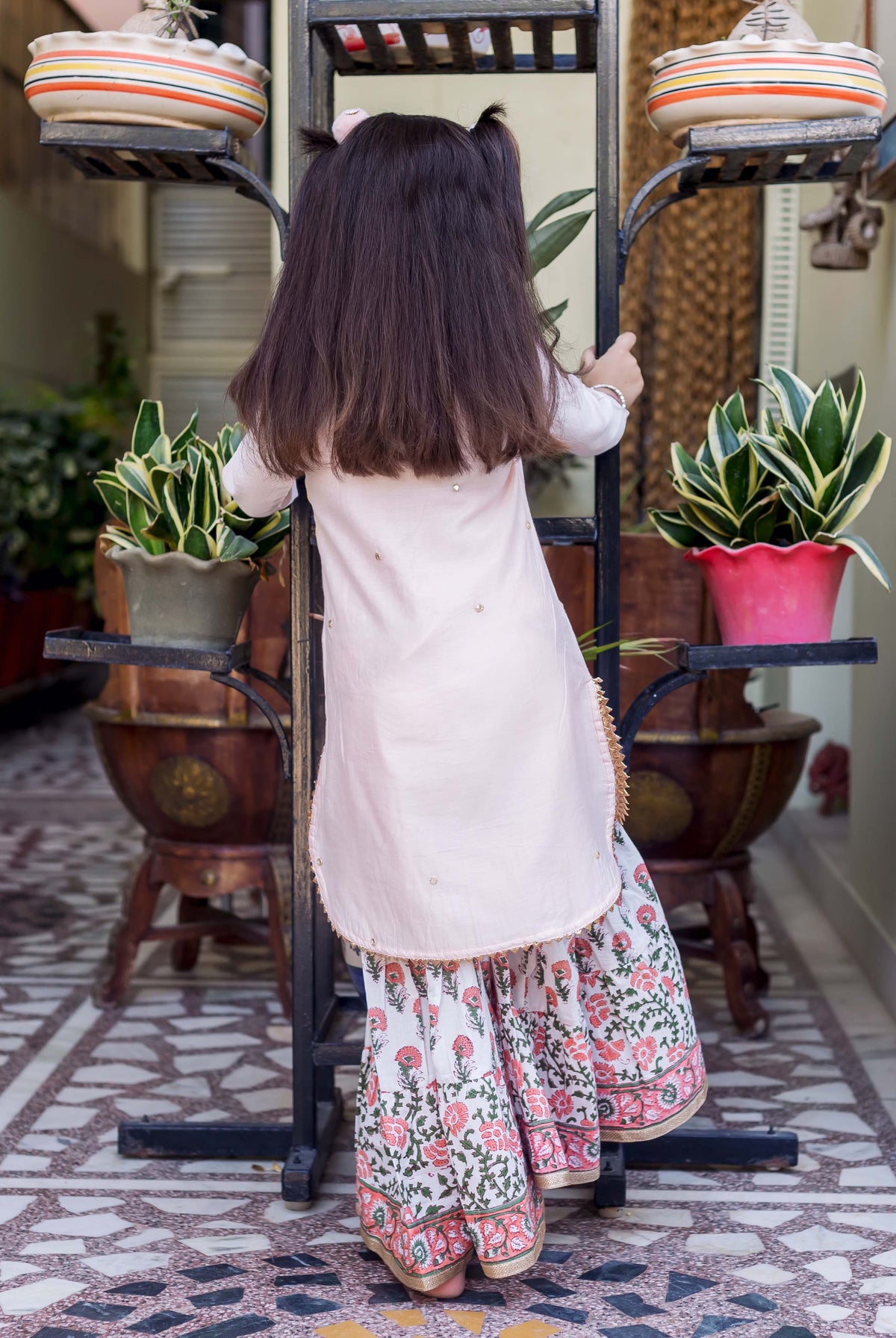 Back view of young girl in light pink embroidered kurta and white floral printed sharara.