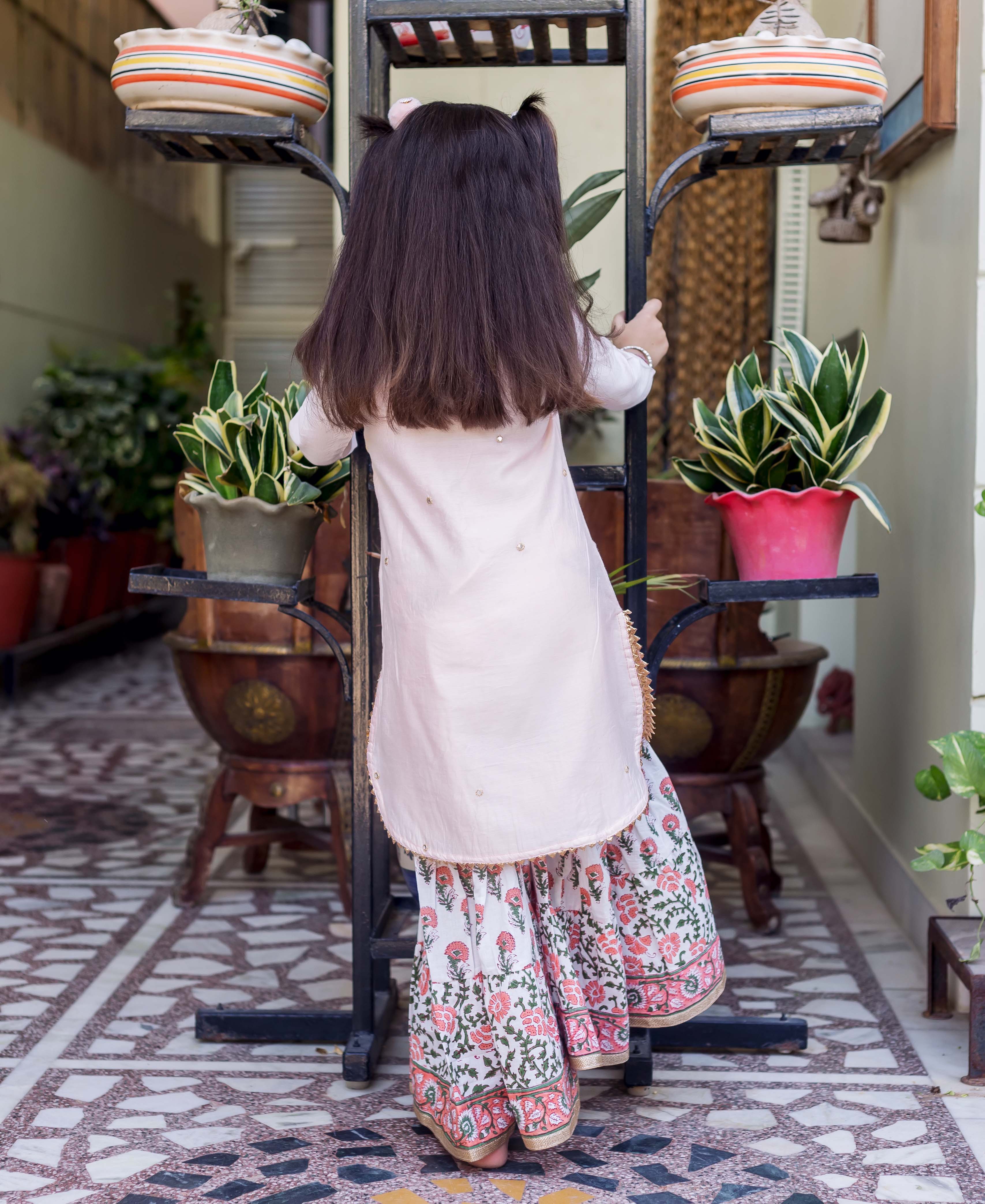 Back view of young girl in light pink embroidered kurta and white floral printed sharara.