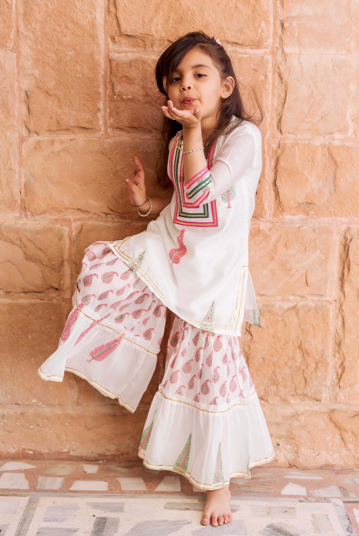 Young girl in white kurta and tiered sharara with pink and green block prints.