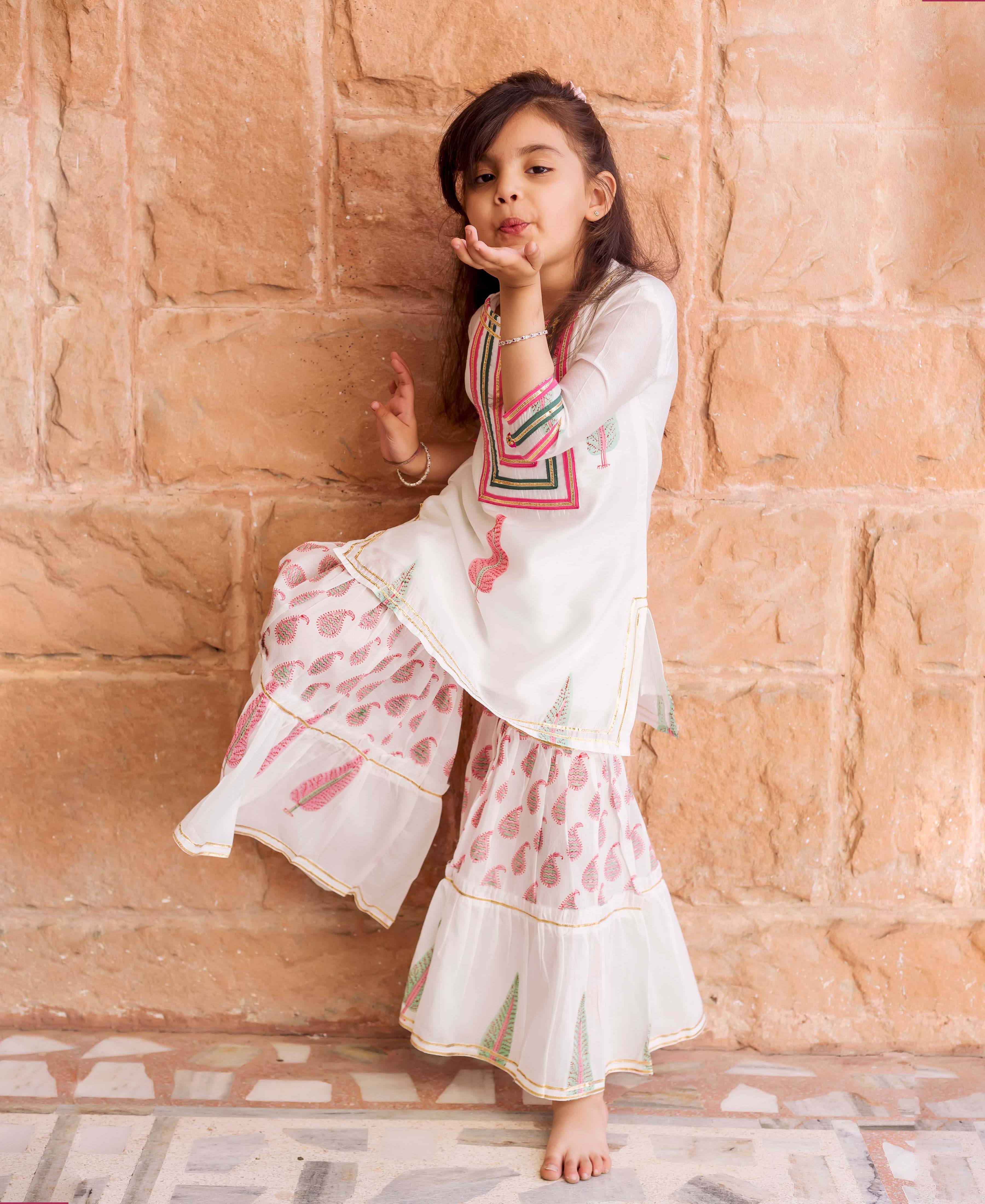 Young girl in white kurta and tiered sharara with pink and green block prints.