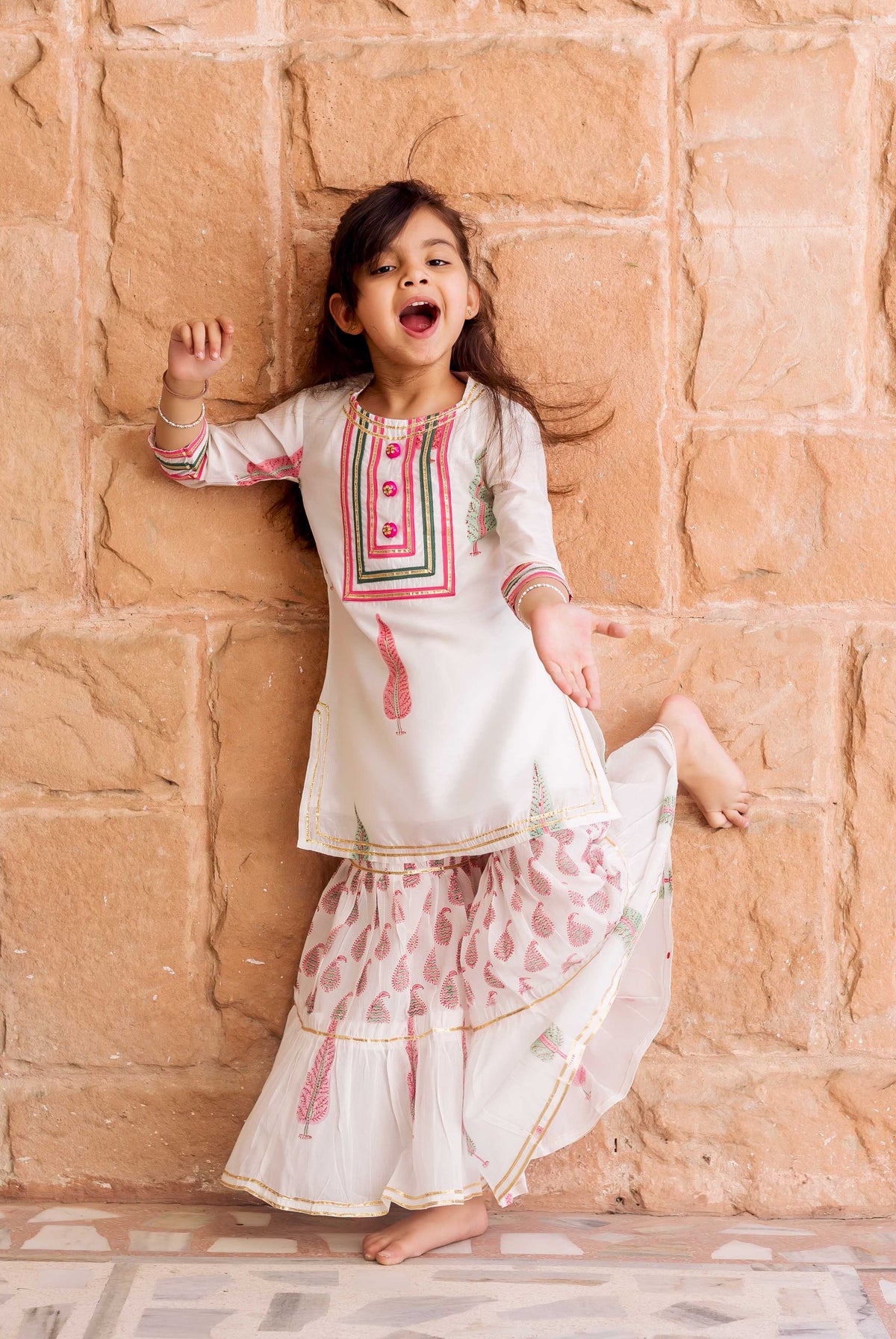 White Chanderi hand-block printed sharara set with pink and green feather motifs on a playful girl.