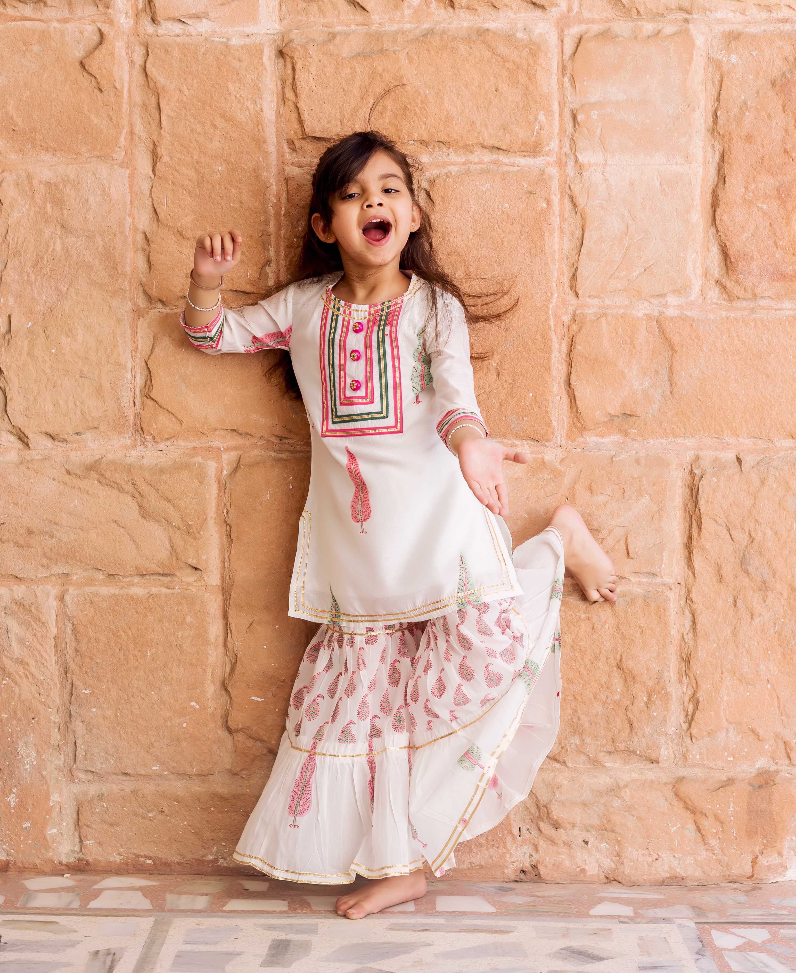 White Chanderi hand-block printed sharara set with pink and green feather motifs on a playful girl.
