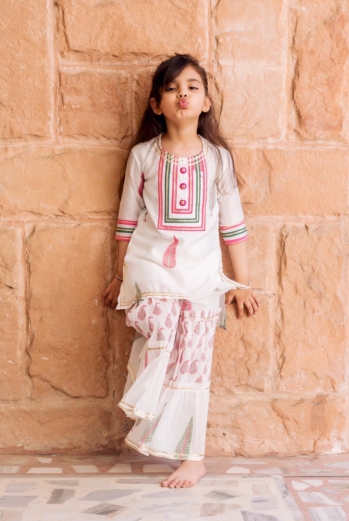 Girl in white sharara set with pink/green geometric and paisley block prints, puckering lips.