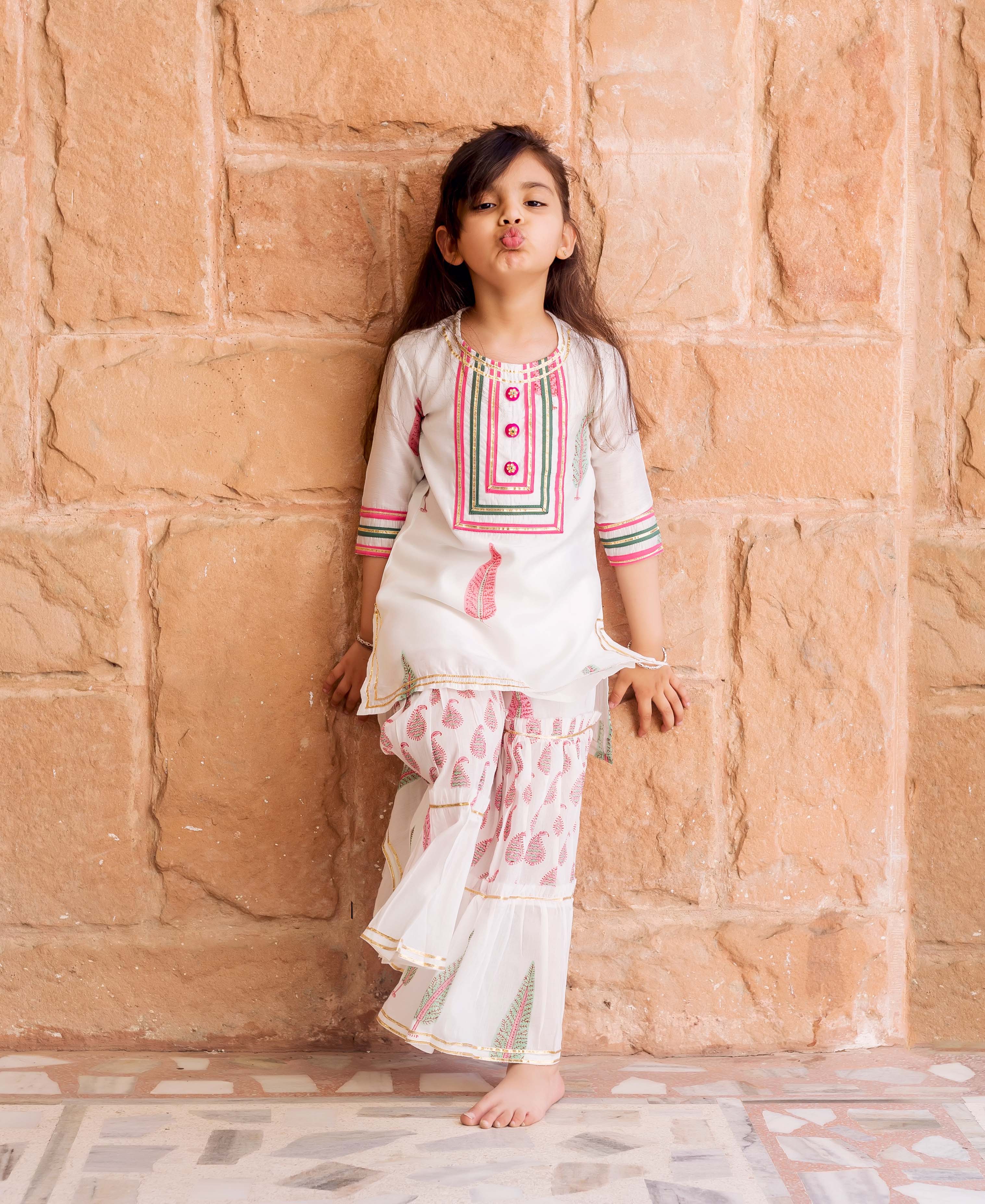 Girl in white sharara set with pink/green geometric and paisley block prints, puckering lips.