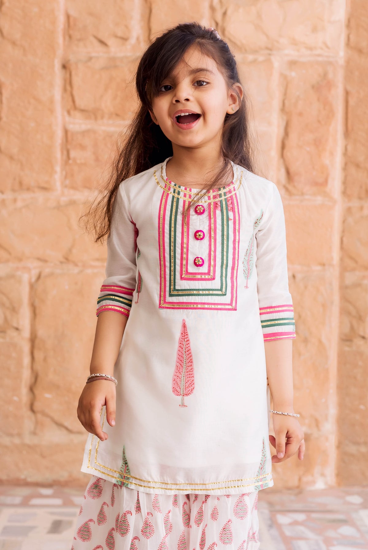 Young girl wearing a white Chanderi sharara set with pink and green block printed patterns.